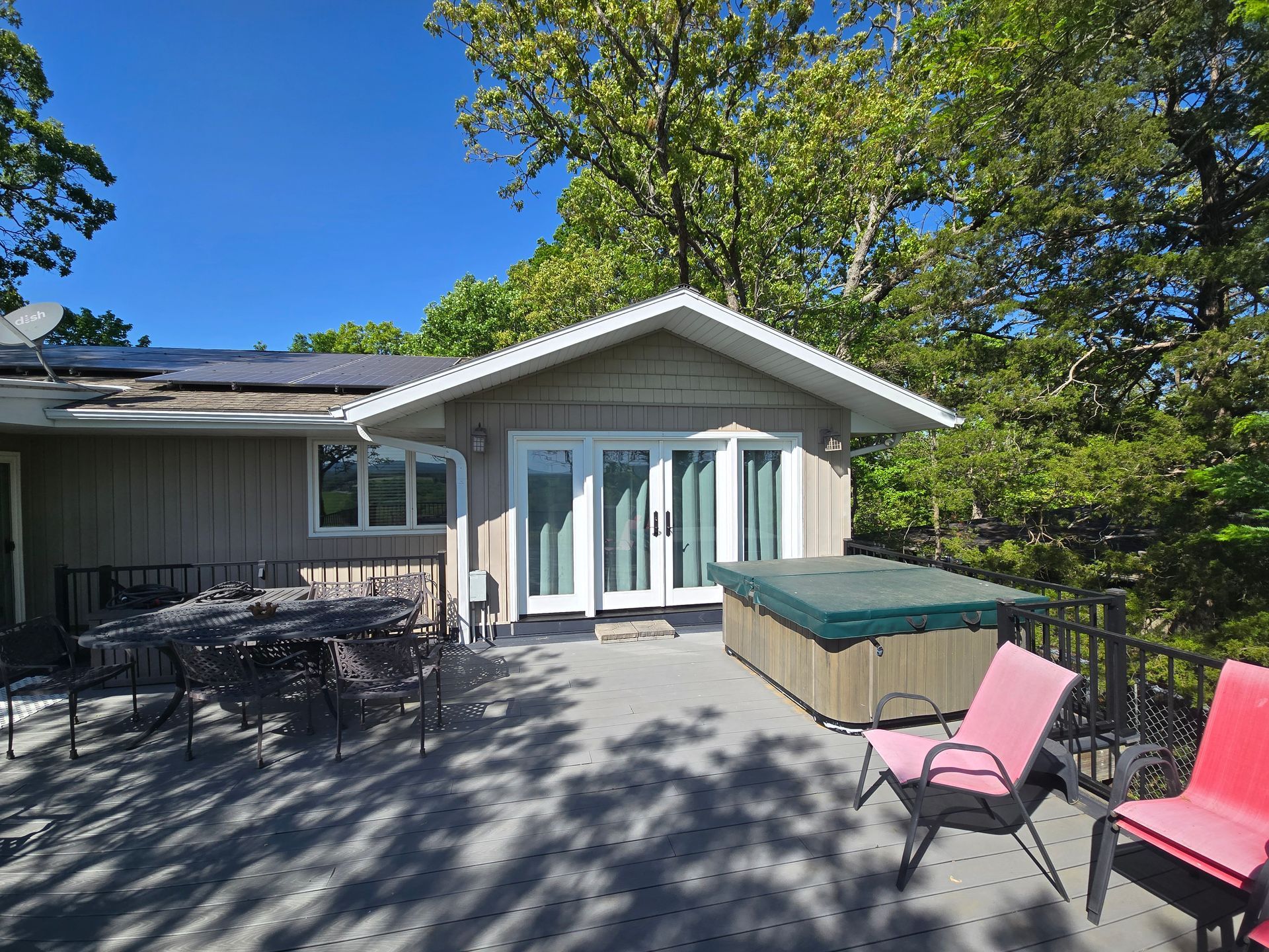 Patio with table and chairs beside a house, green hot tub, and pink lounge chairs under trees