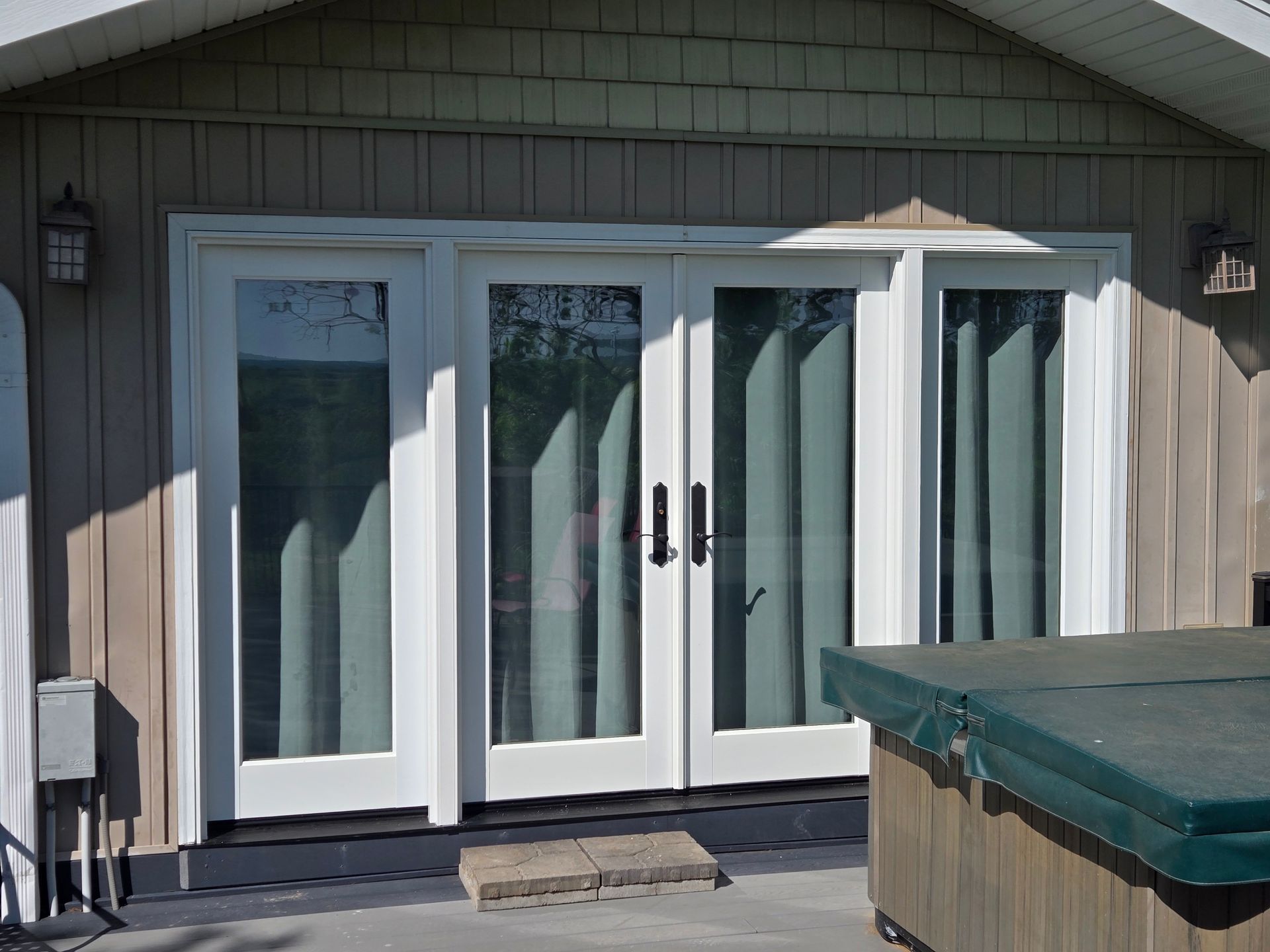 White French doors on a house deck, with a green hot tub cover in the foreground.