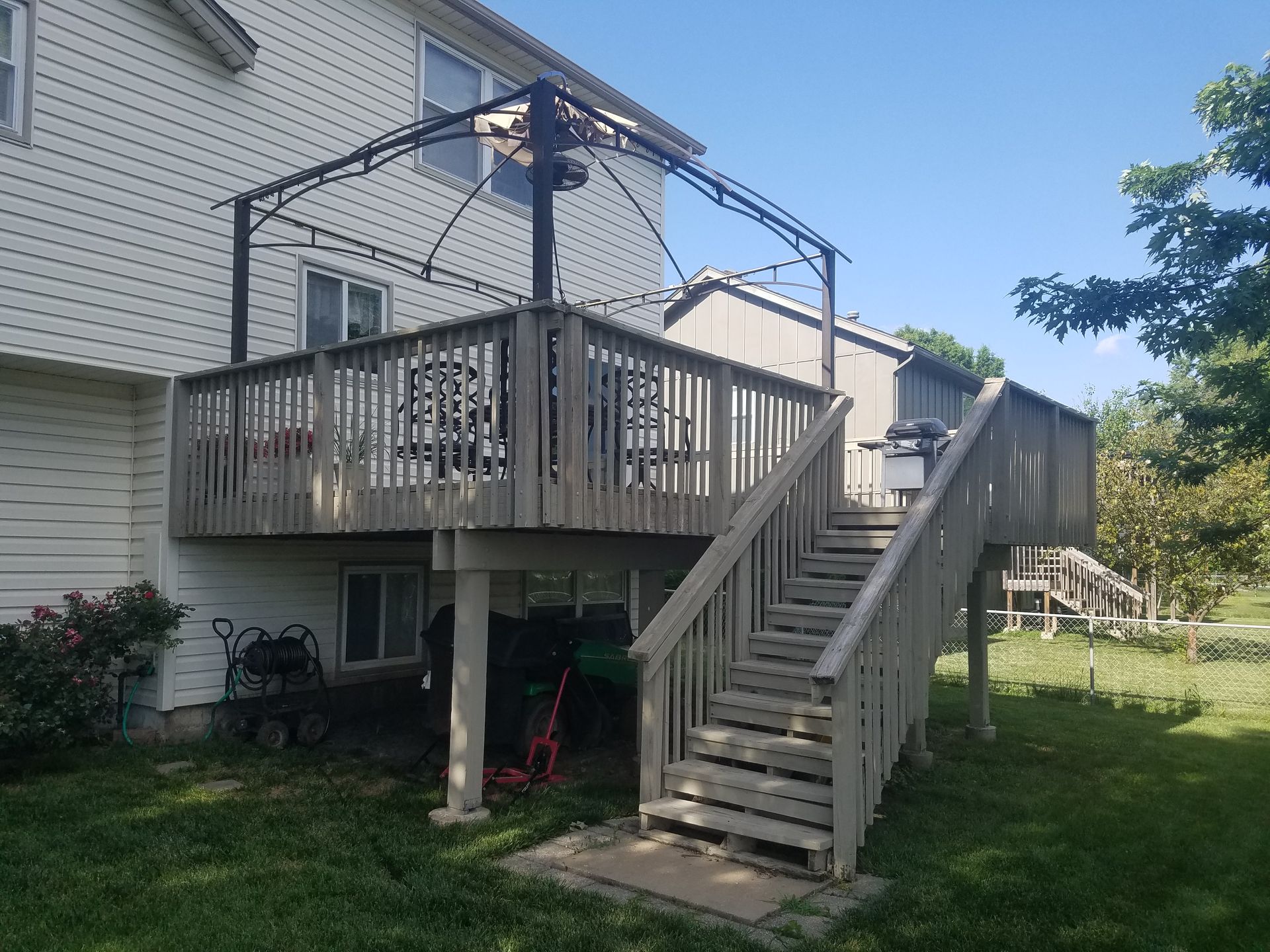 Backyard deck with stairs, railing, and overhead swing frame beside a house