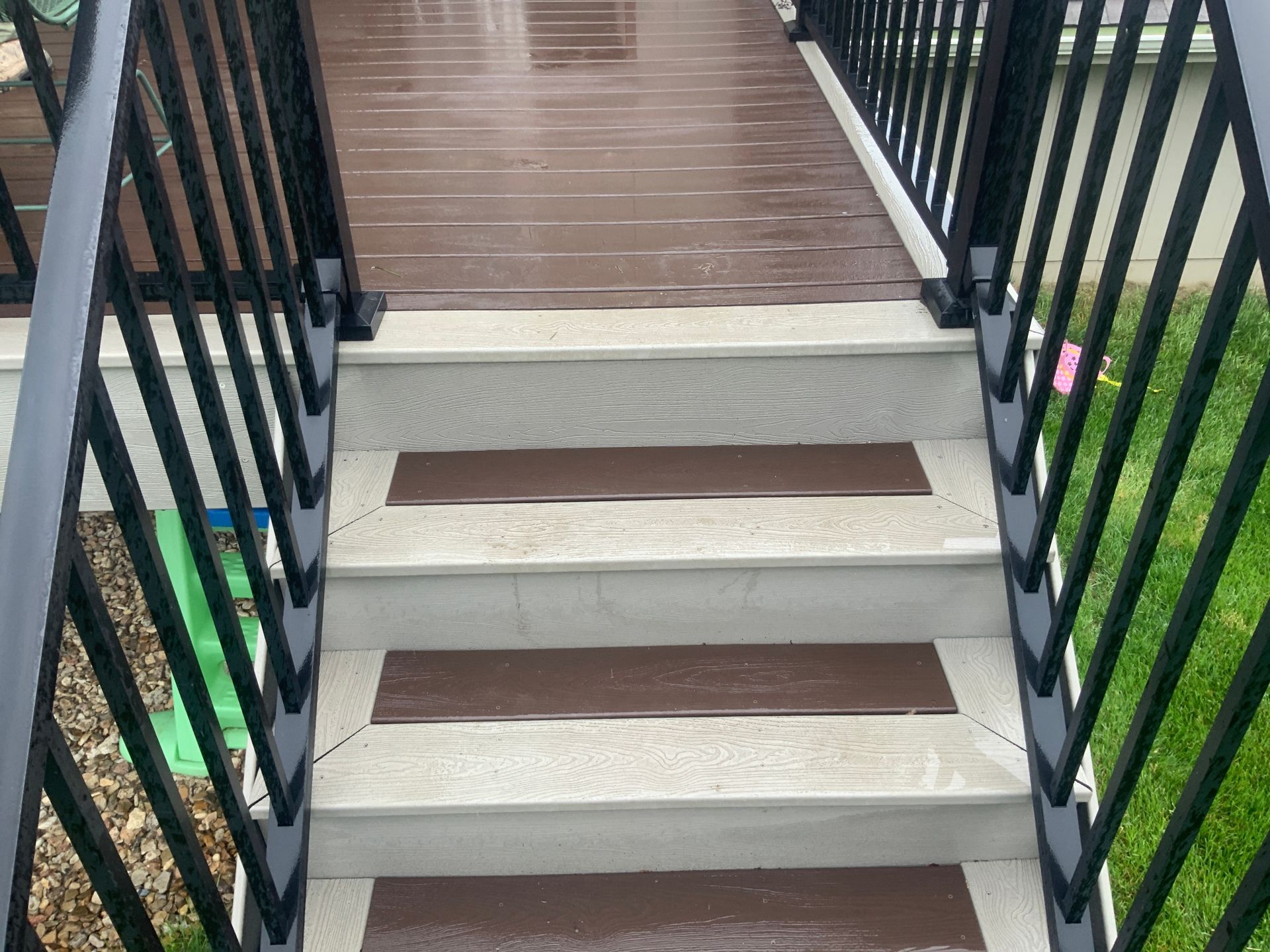 Narrow outdoor staircase with white steps, brown treads, and black railings leading up to a deck