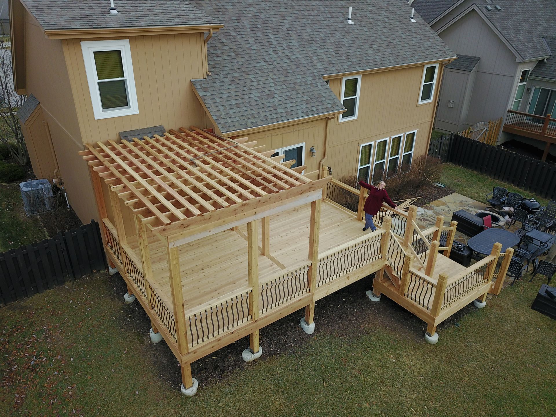 Backyard deck under construction beside a house, with a worker on the railing and framing exposed.