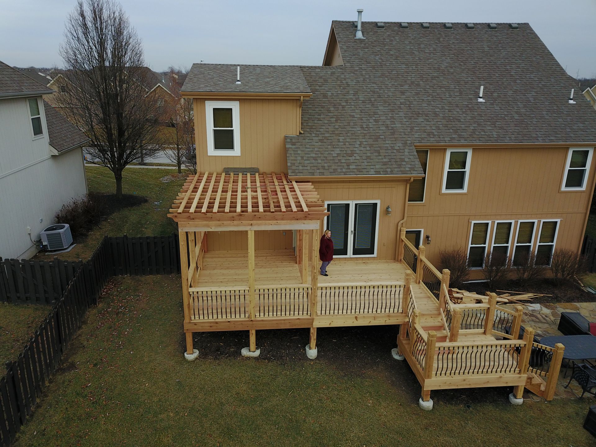 Backyard view of a house with a wooden deck, pergola, and stairs