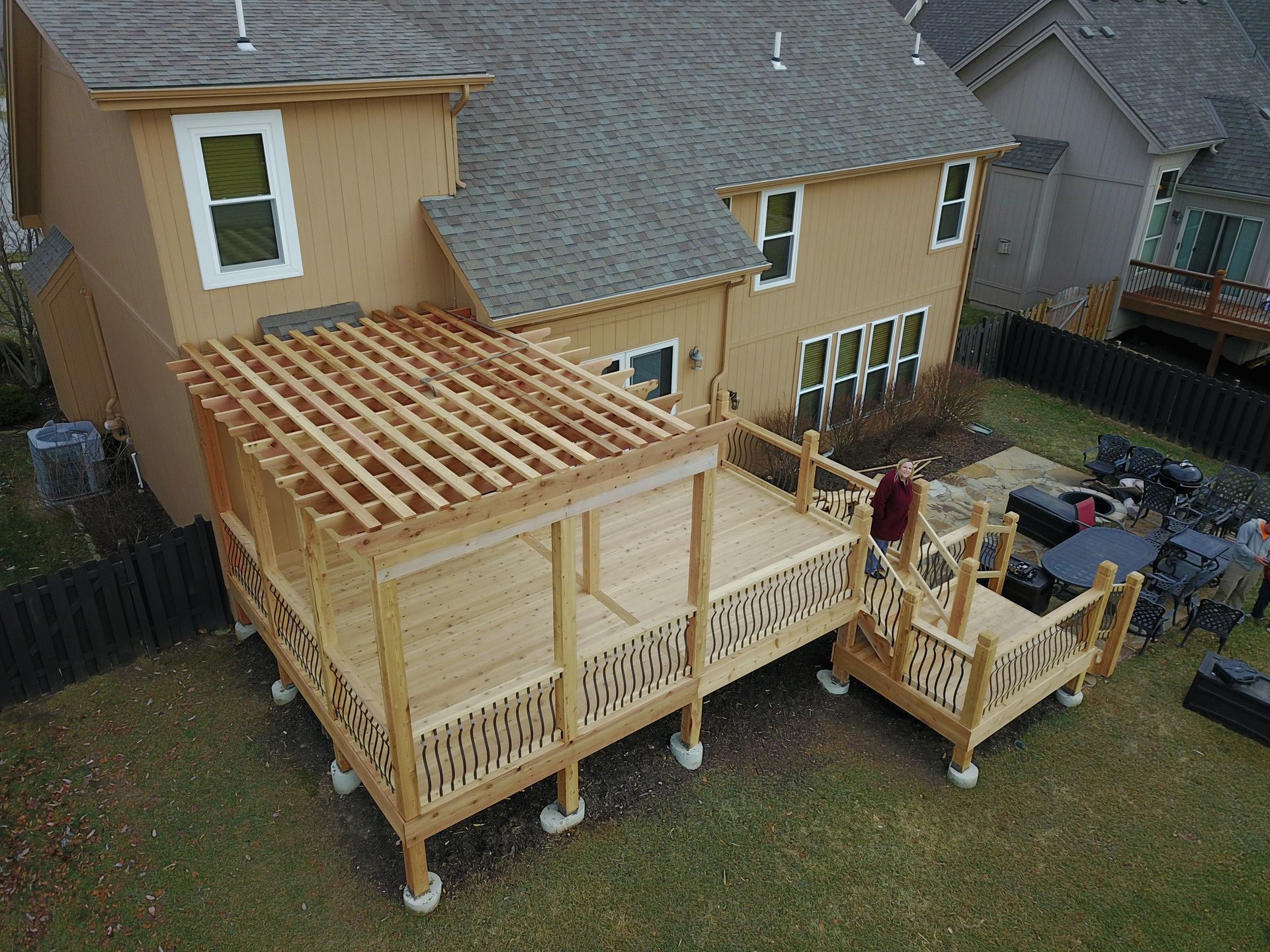 Backyard wooden deck under construction beside a yellow house, with pergola framing and stairs on the right.