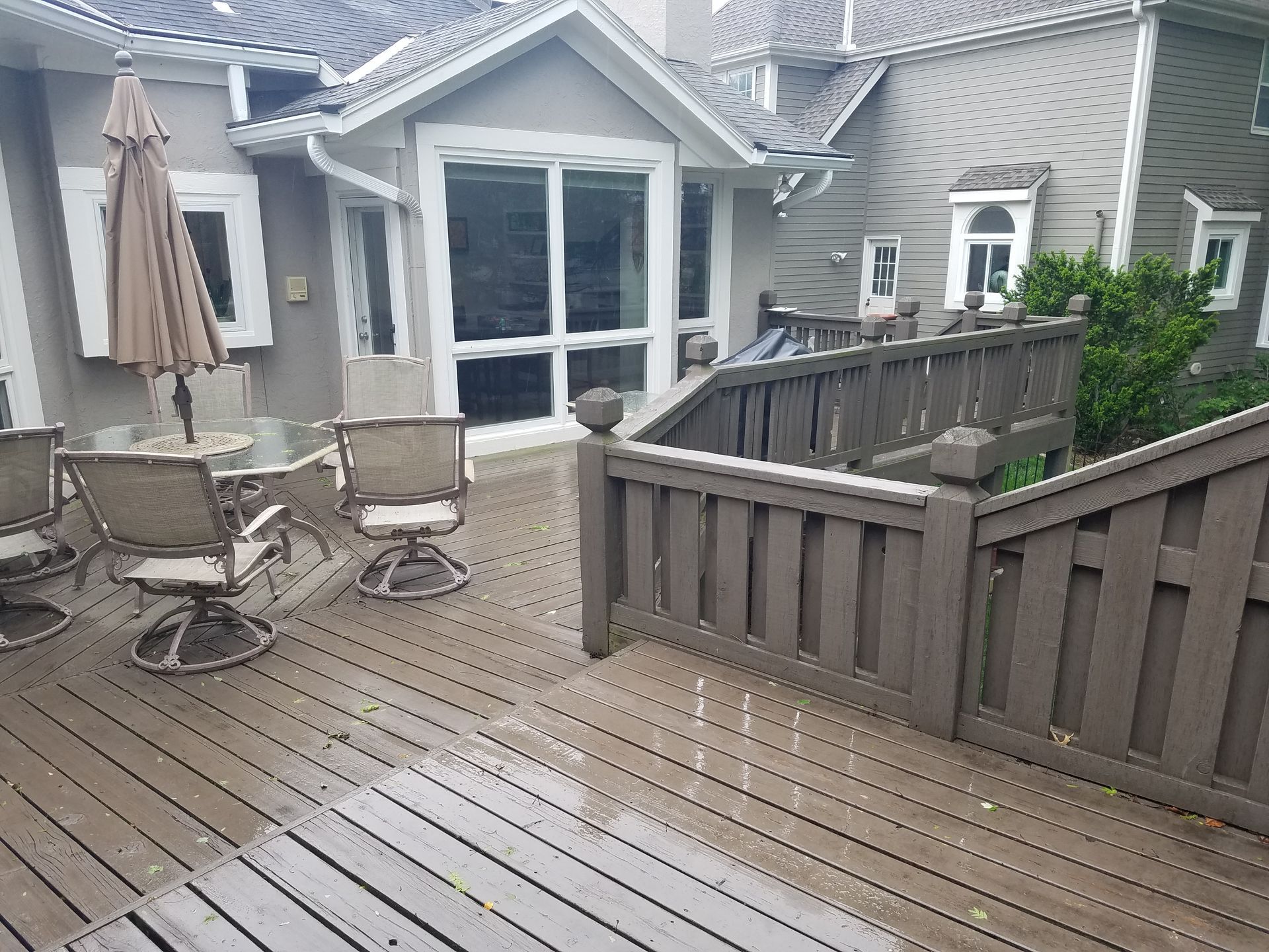 Wooden backyard deck with patio table, chairs, umbrella, and a railing beside a house.