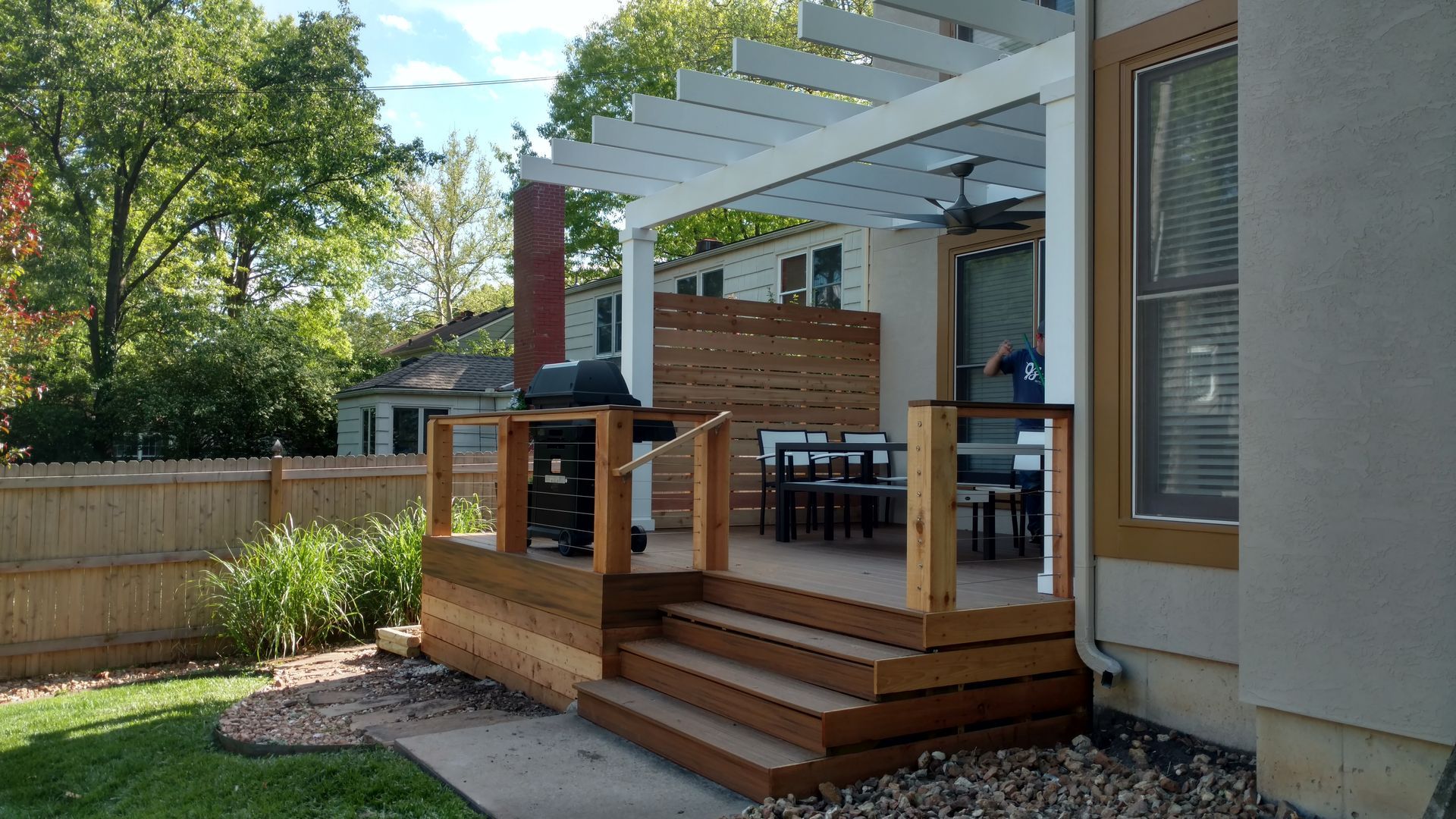 Backyard wooden deck with pergola, steps, outdoor seating, and potted plants beside a house