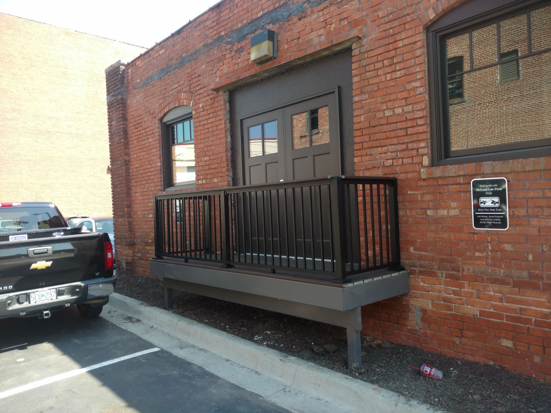 Brick building entrance with black railing and small ramp beside parked pickup truck