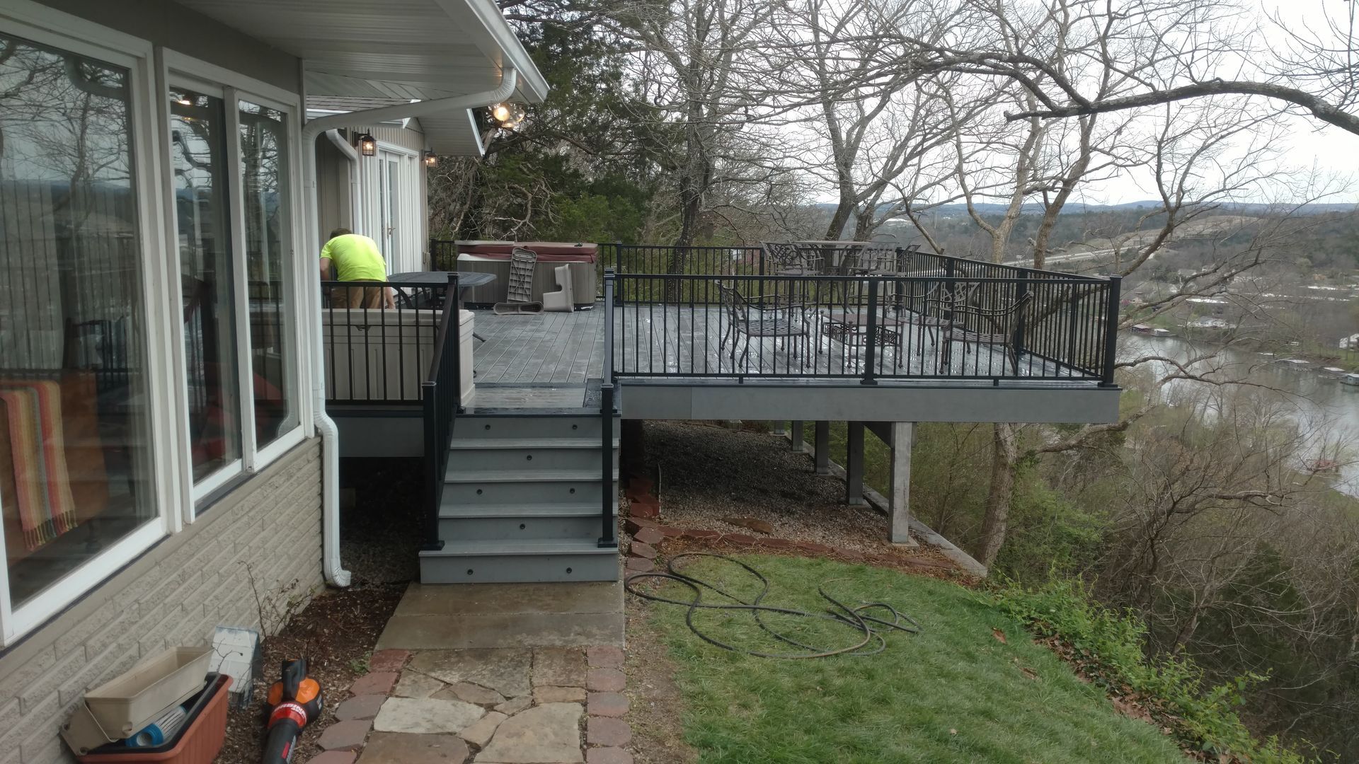 Patio deck with stairs beside a house, overlooking a grassy yard and wooded hillside.