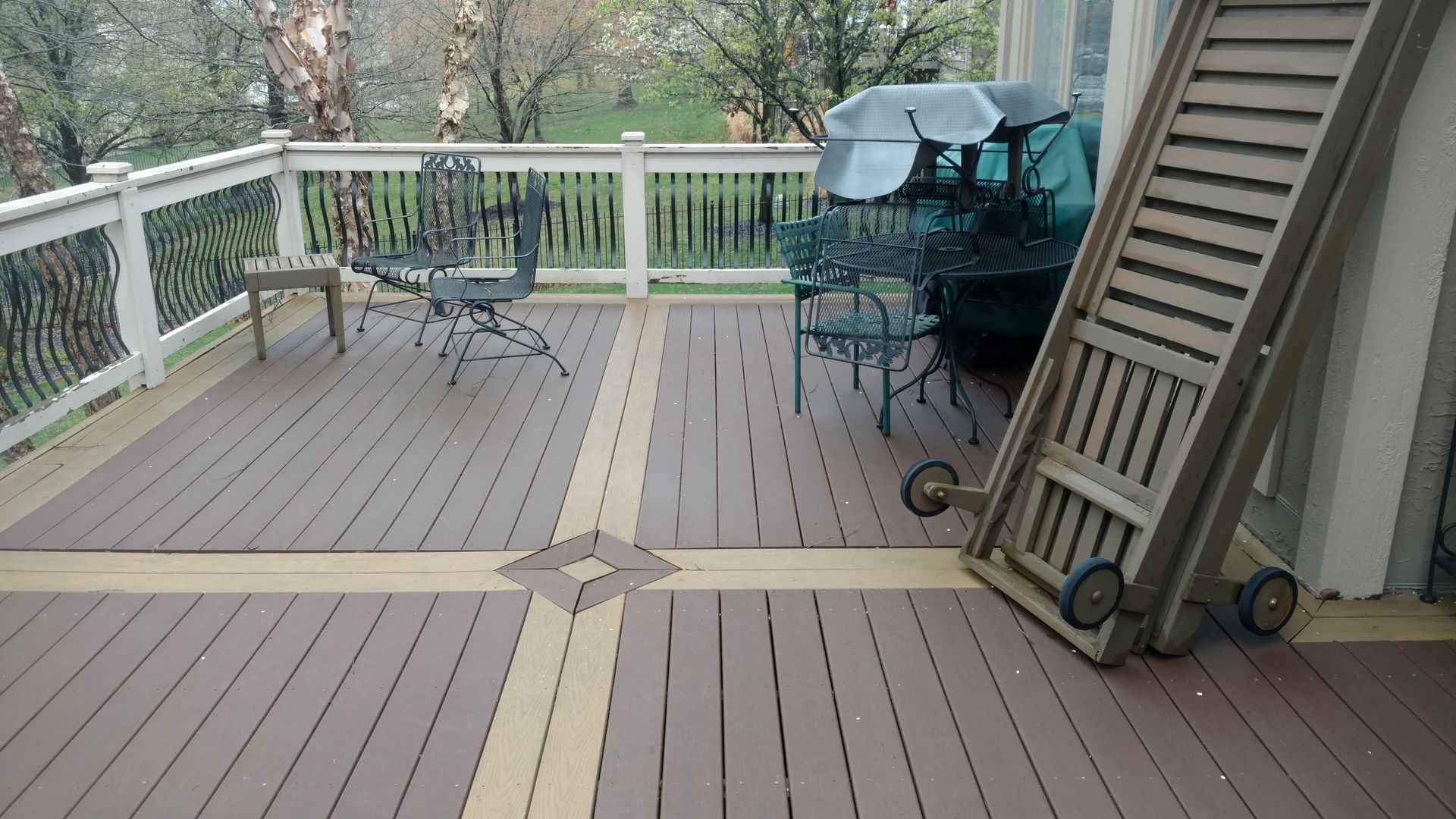 Wooden deck with patio furniture, railings, and a grill in a backyard.