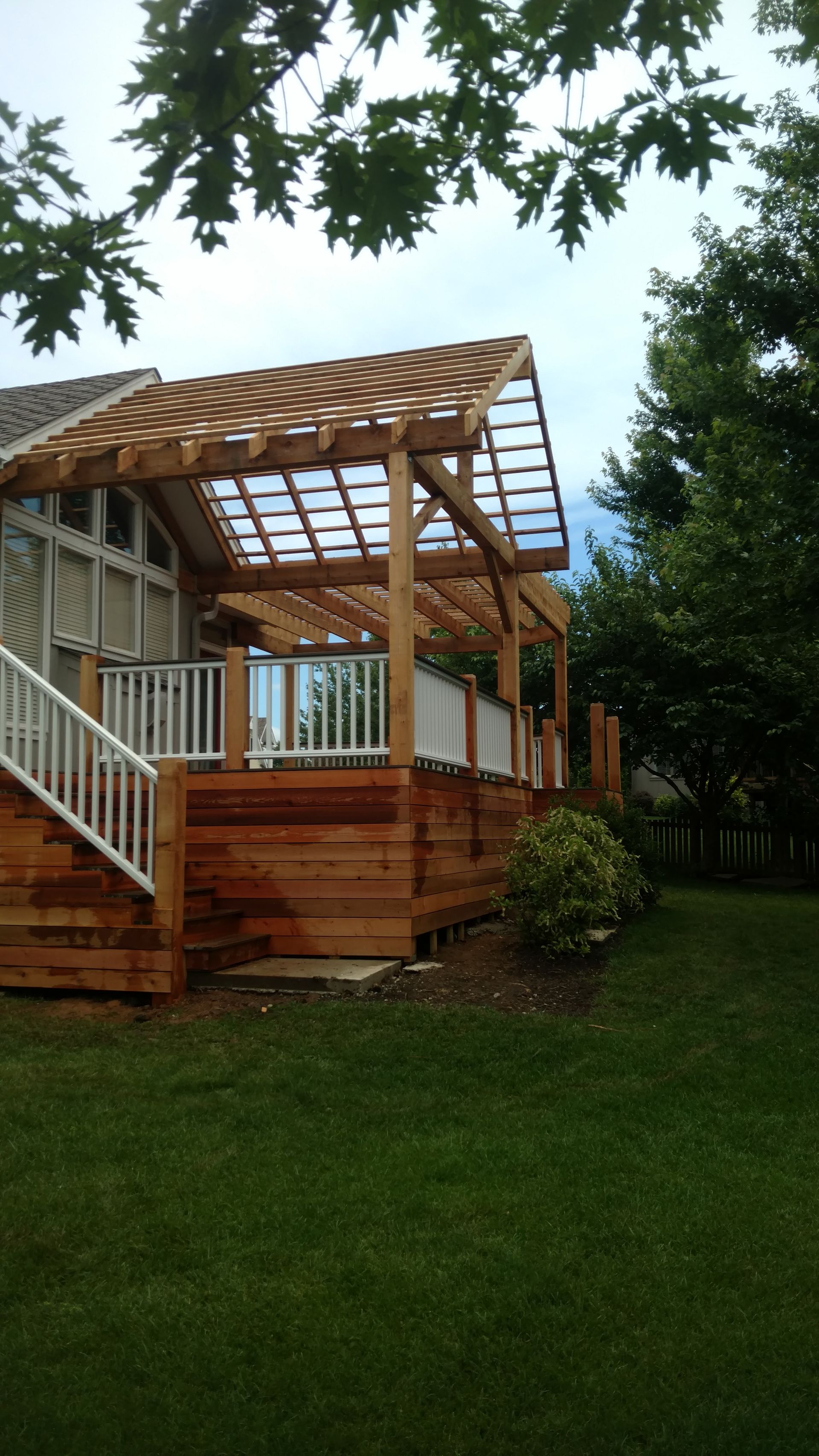 Wooden backyard deck with railings and a partially built pergola beside a grassy yard.