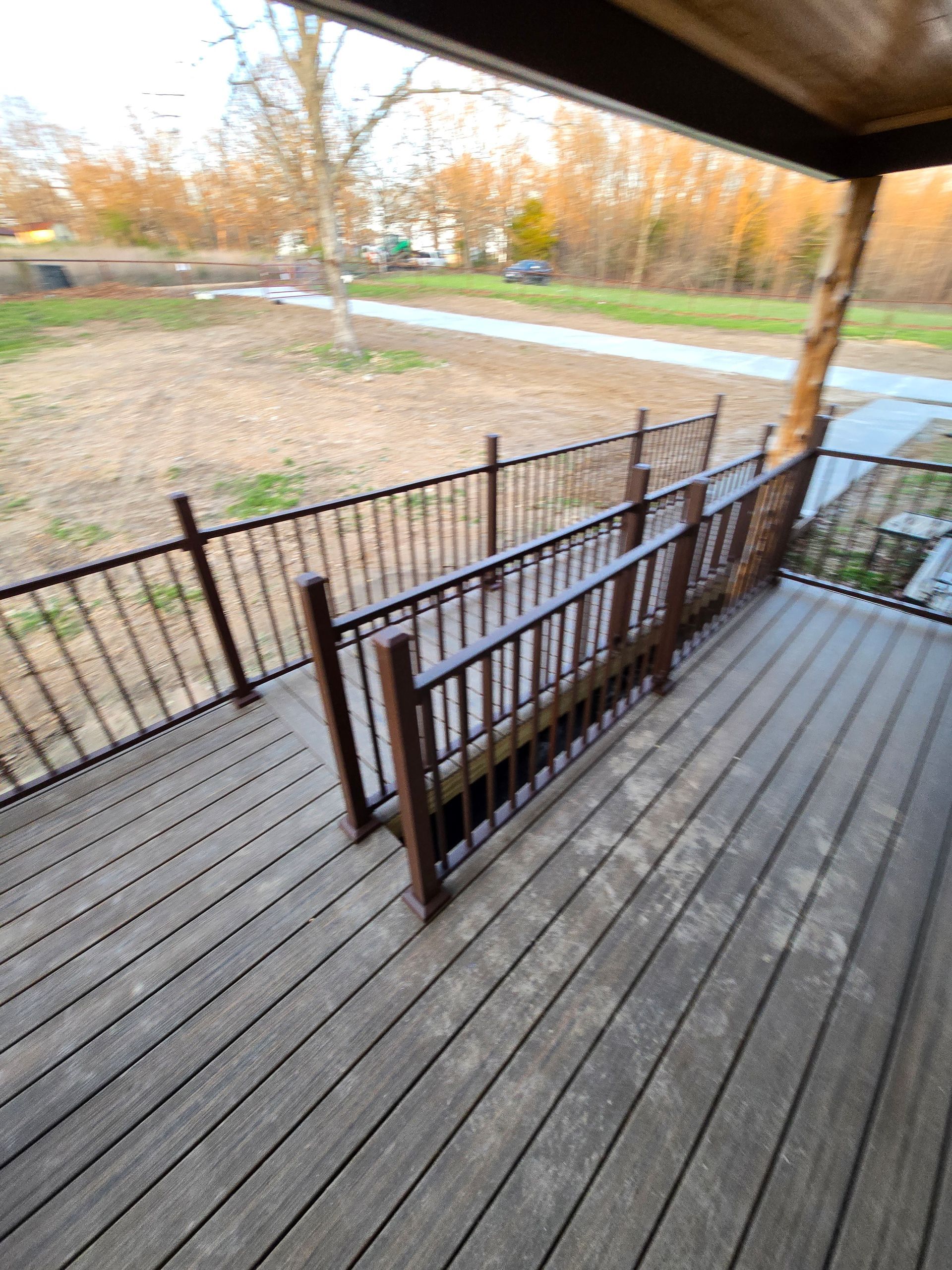 Wooden porch deck with black railing overlooking a yard and sidewalk in autumn.