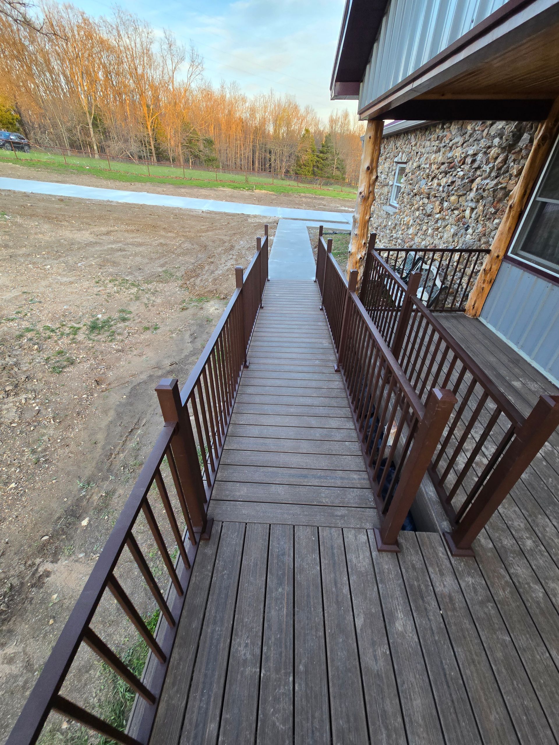 Wooden ramp with railings leading from a porch to a grassy yard near trees and a paved path