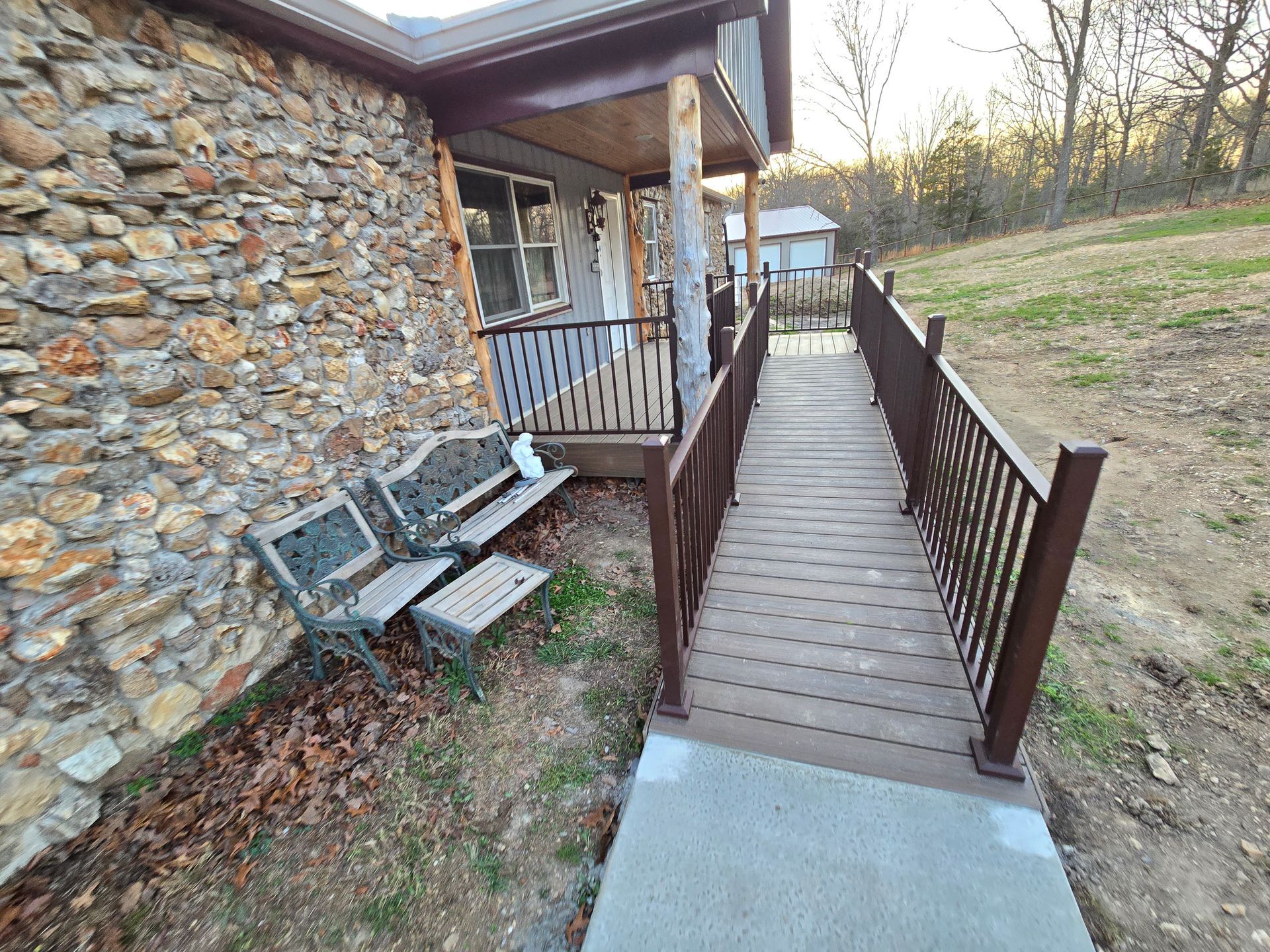 Wooden accessibility ramp beside a stone building, with brown railings and steps leading uphill.