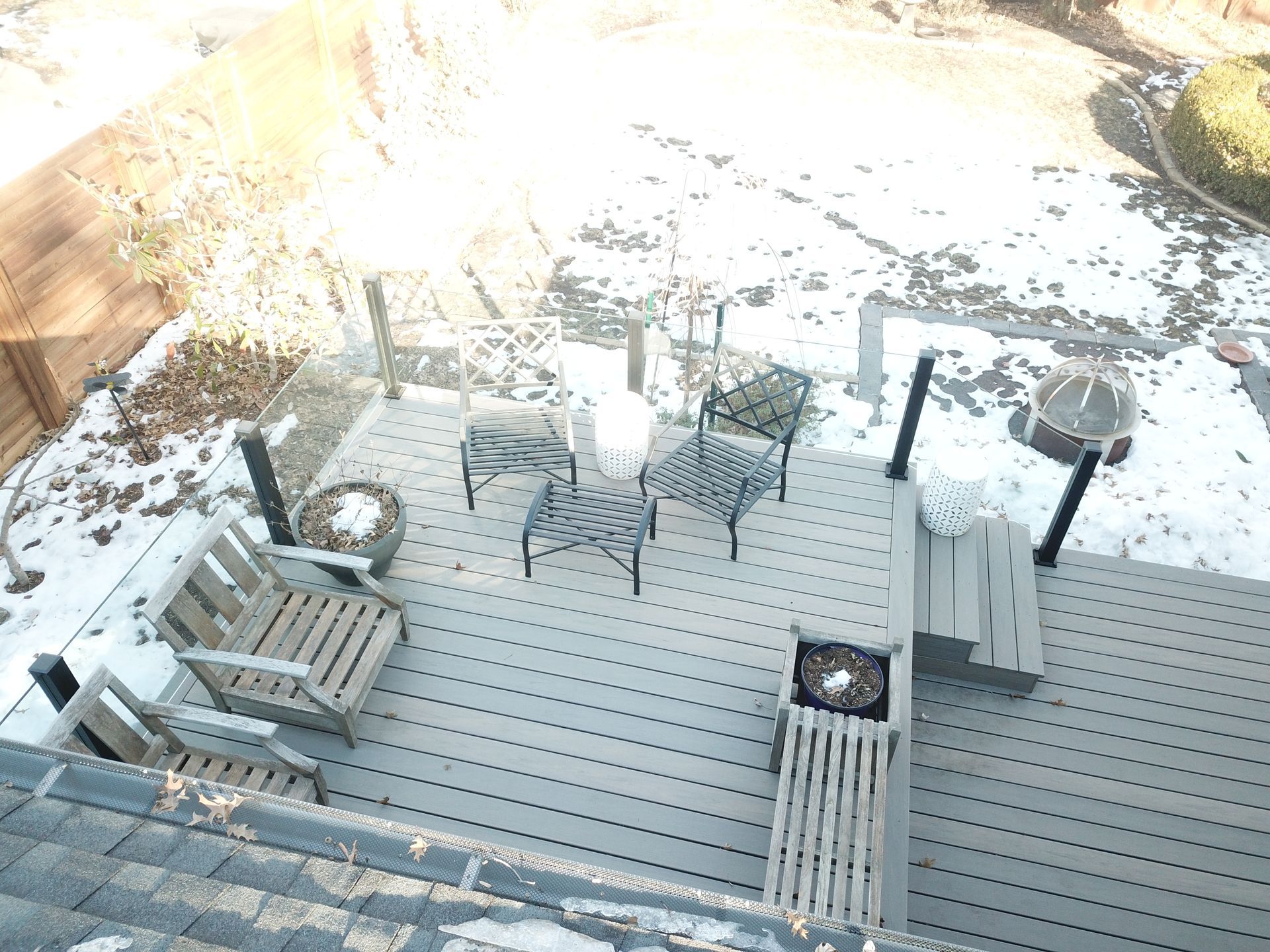 Snowy backyard deck with patio table, chairs, benches, and a grill in winter sunlight