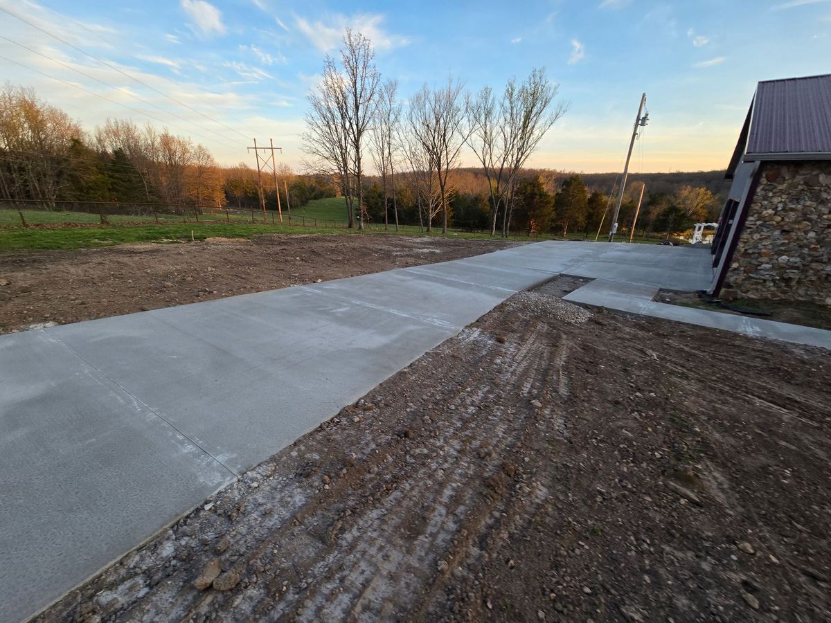 Freshly poured concrete driveway beside a house, leading across a yard at sunset