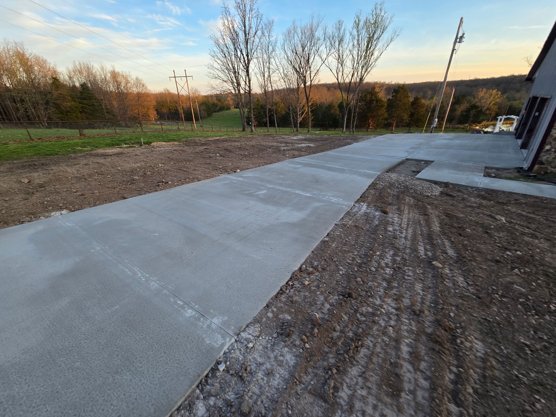 New concrete walkway beside a building at sunset, with grassy field and trees nearby