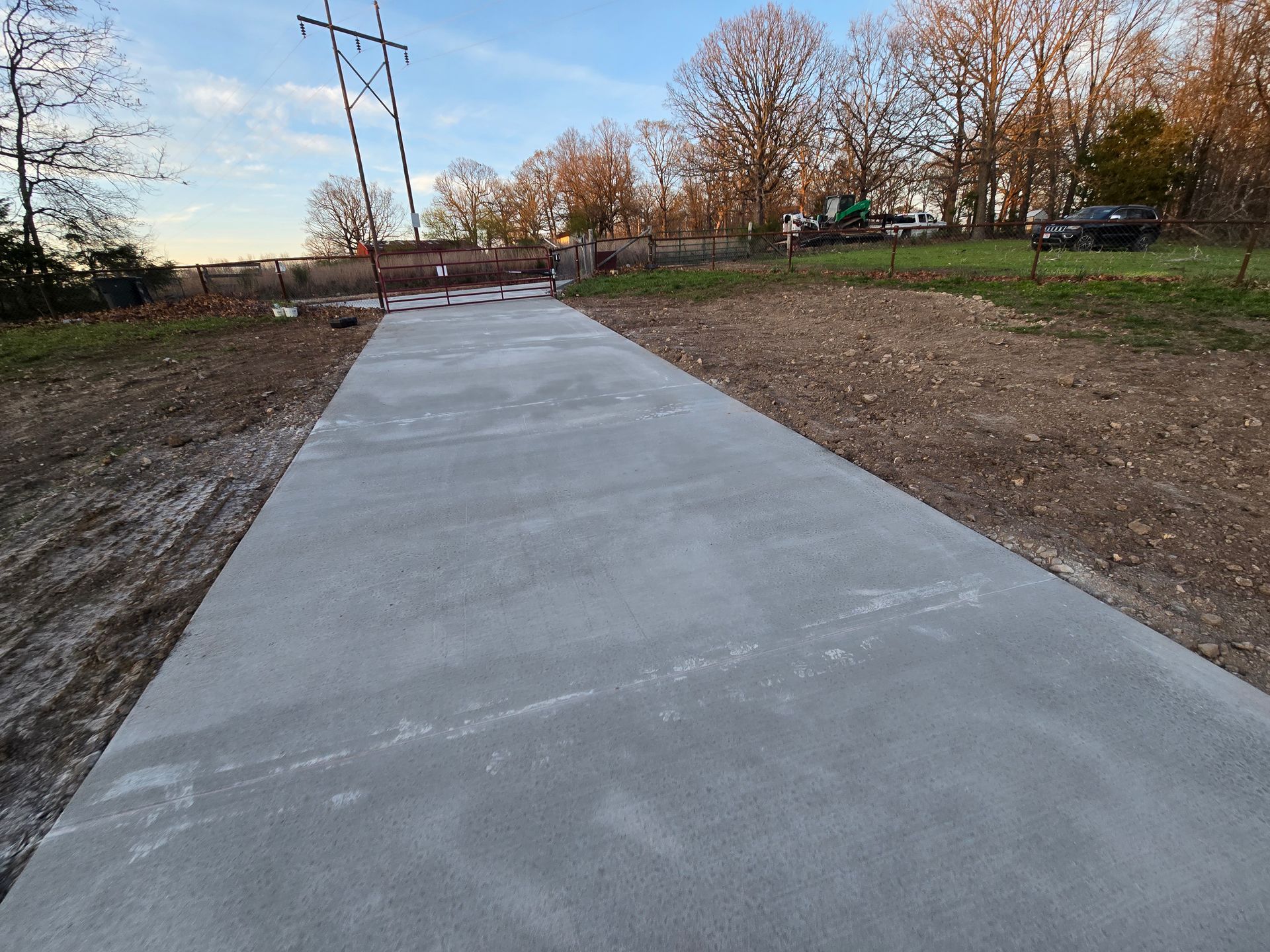 New concrete path through a park with trees and power lines at dusk