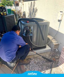 Technician crouches beside a rooftop HVAC unit, inspecting equipment with a flashlight.