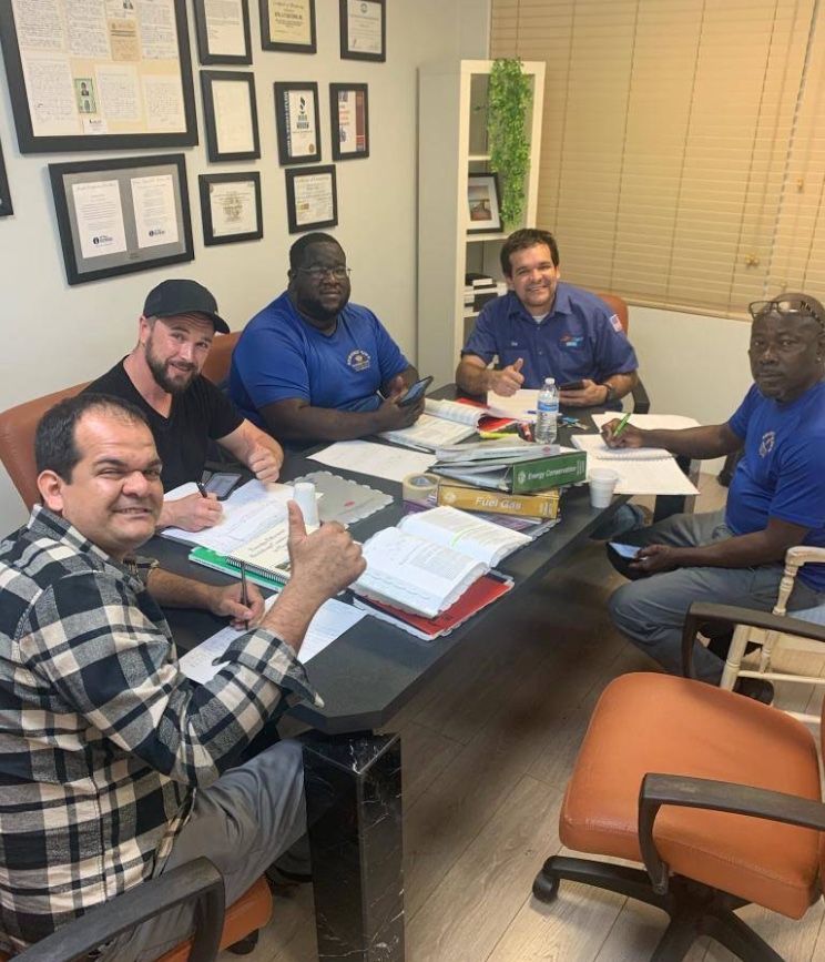 Five people sit around a conference table in an office, reviewing papers and books during a meeting.