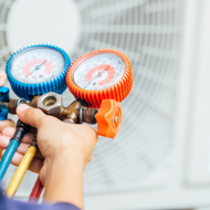 Hands holding manifold gauges with blue and orange dials for air conditioning service