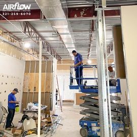 Workers installing ceiling ductwork in a commercial interior with scaffolding and tools.