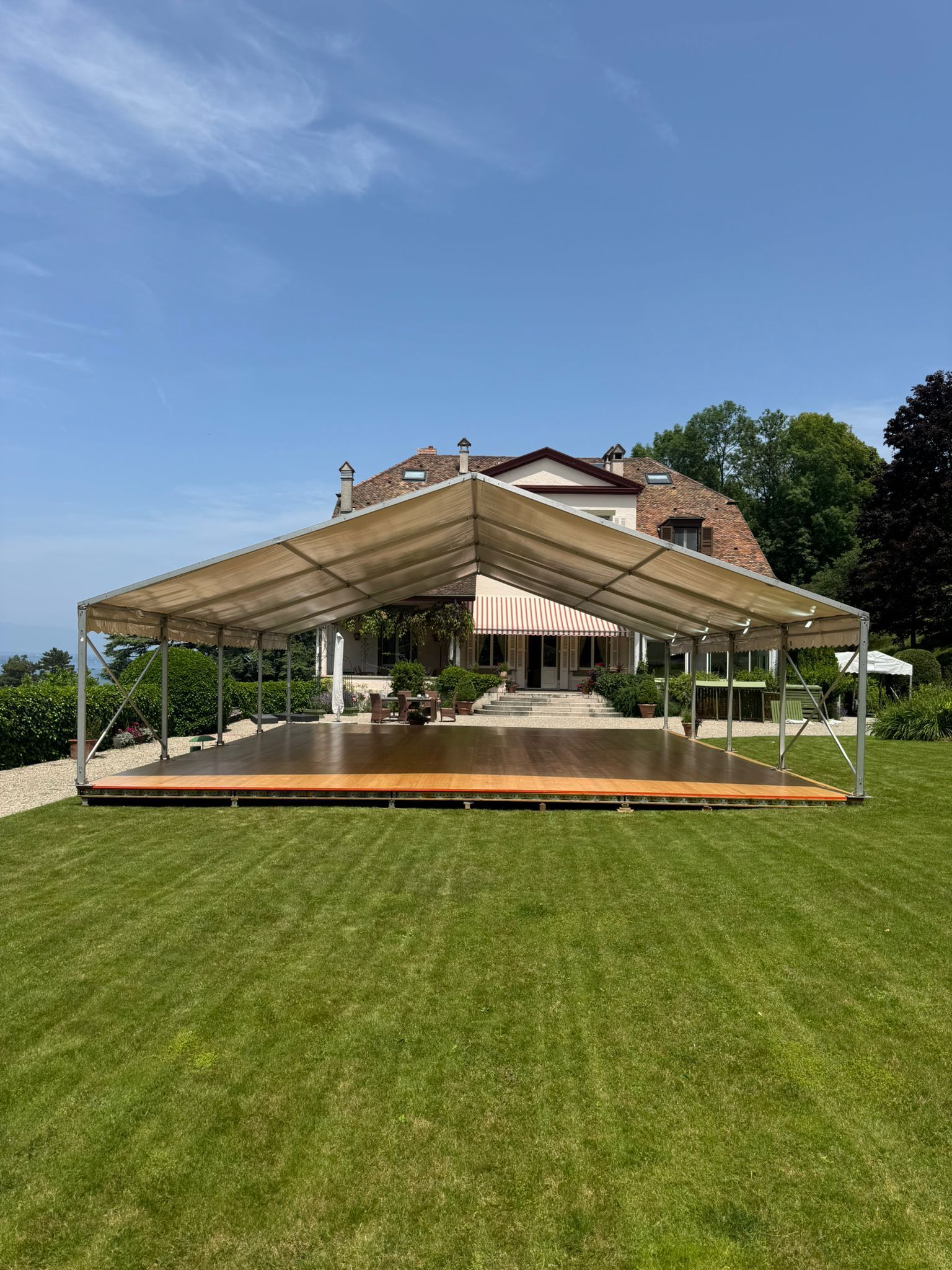 Une tente dressée sur une pelouse devant une maison, sous un ciel bleu.