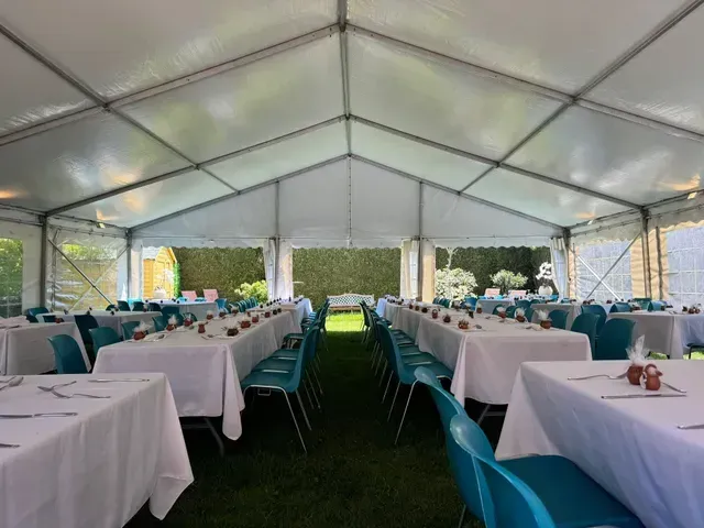 Sous une tente blanche, des tables sont dressées sur l'herbe verte pour un événement sur le thème turquoise.