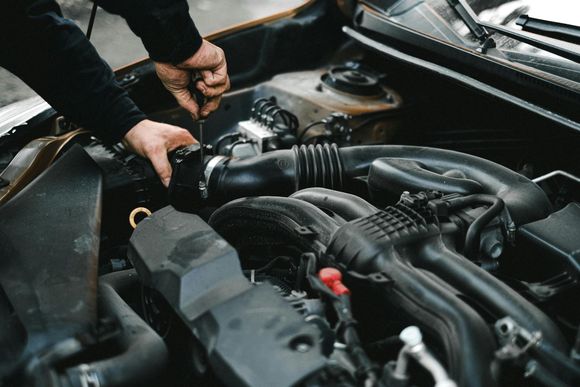 A close-up view of hands using a screwdriver to perform maintenance on a car engine.