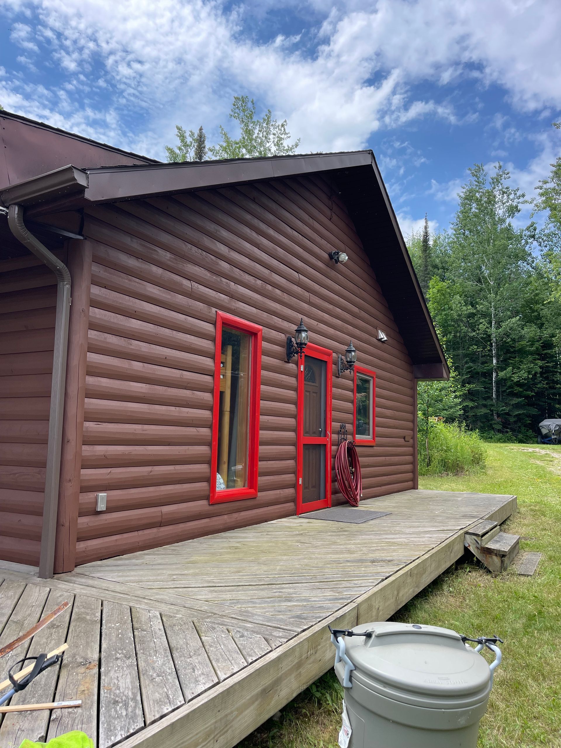 A log cabin with a wooden deck and a toilet in front of it.