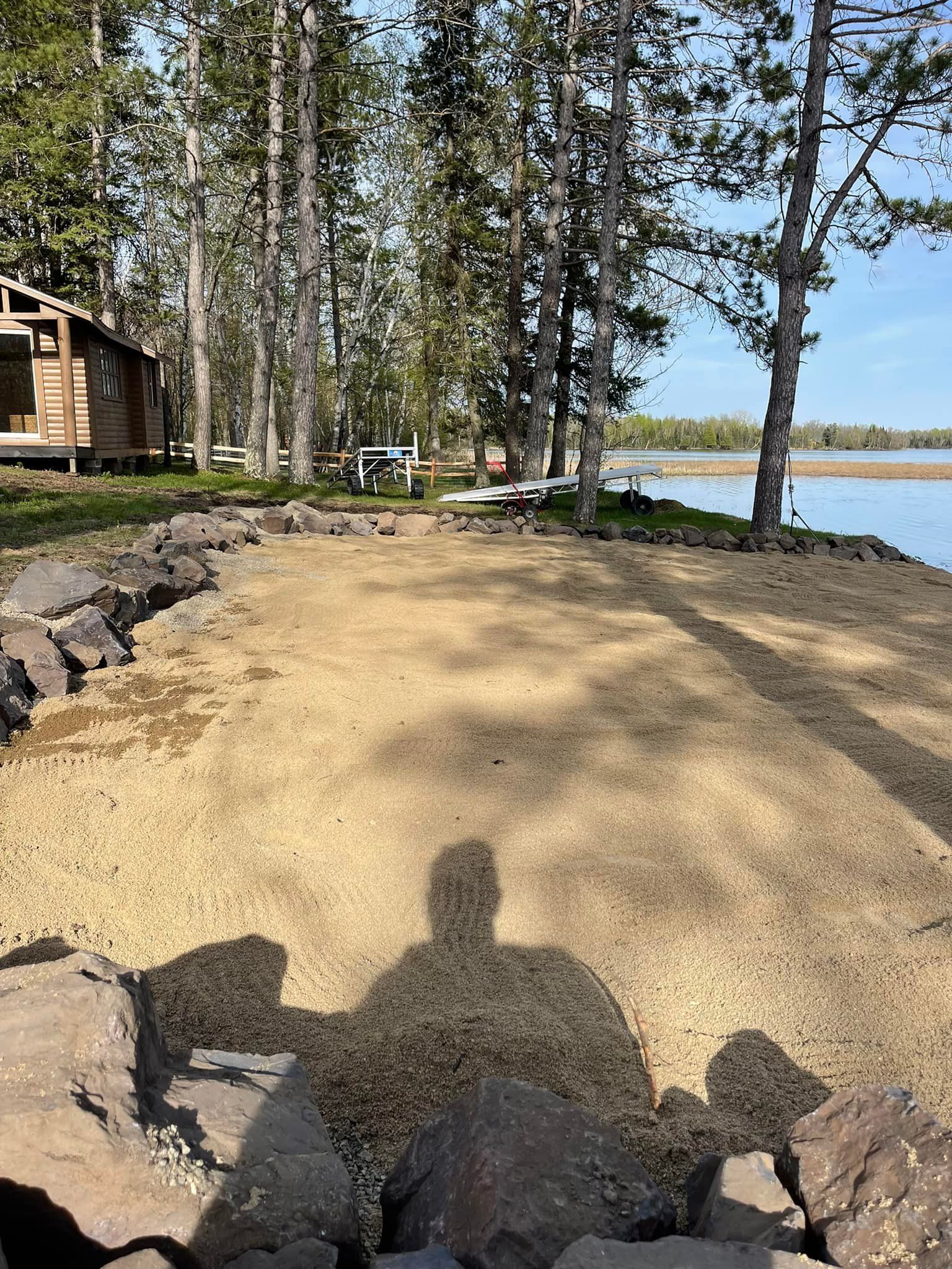 A shadow of a person is cast on the ground near a lake.