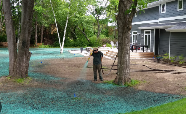 A man is spraying green fertilizer on a lawn in front of a house.