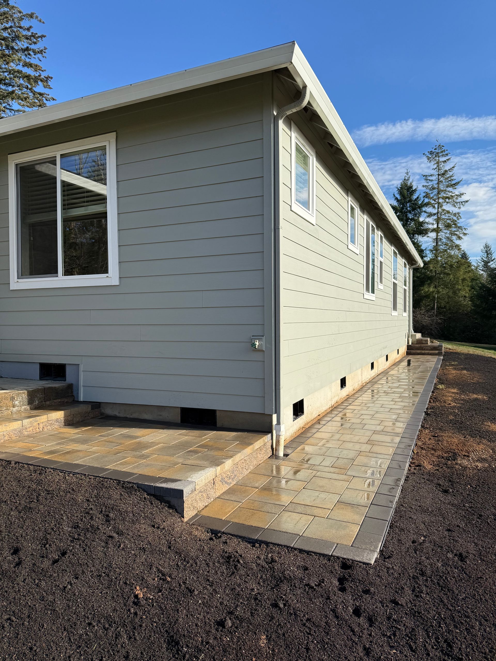 Gray house with white trim and a paved walkway in a wooded setting.