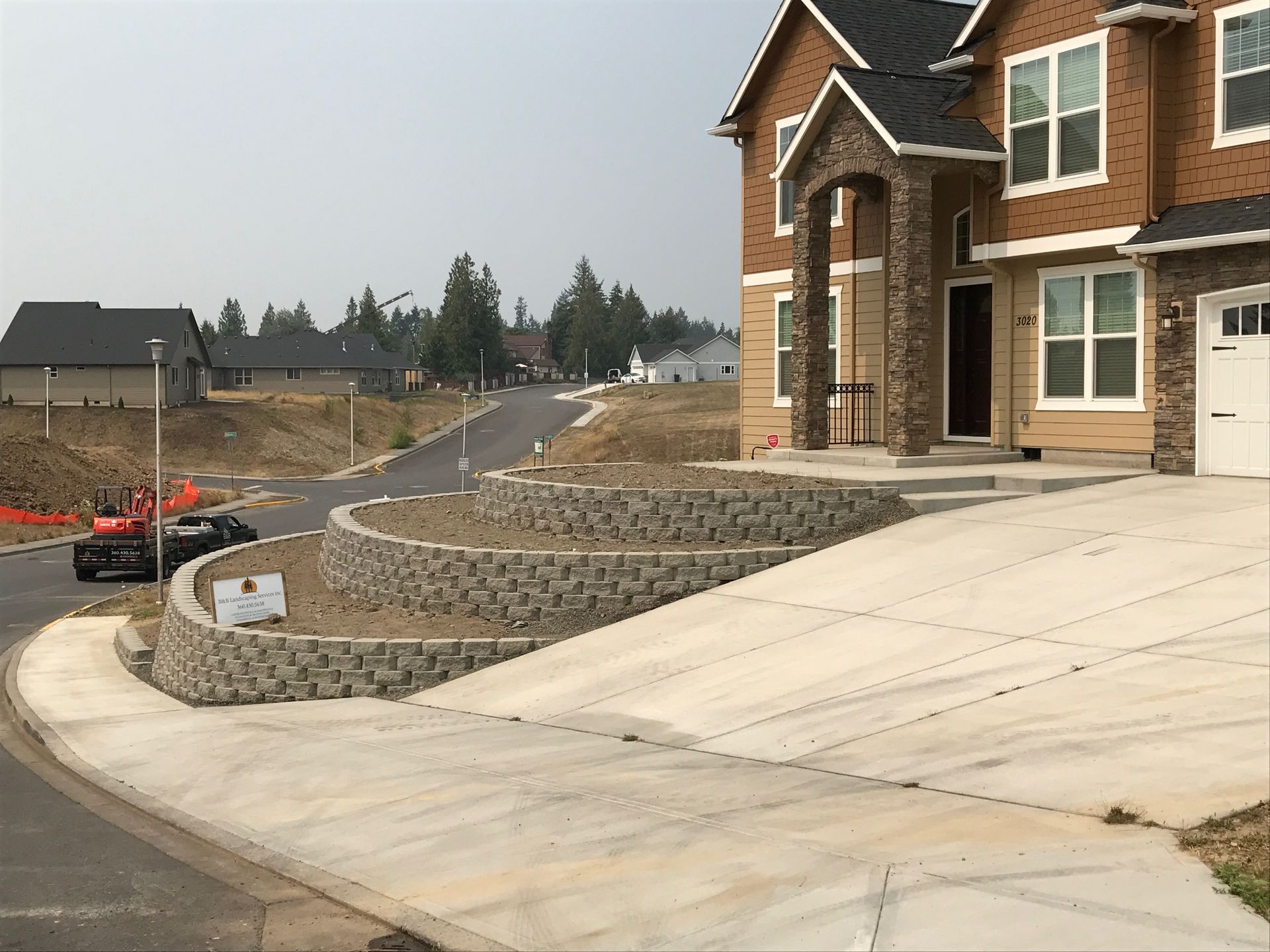 A two-story house with a tiered retaining wall along a driveway on a slight incline.