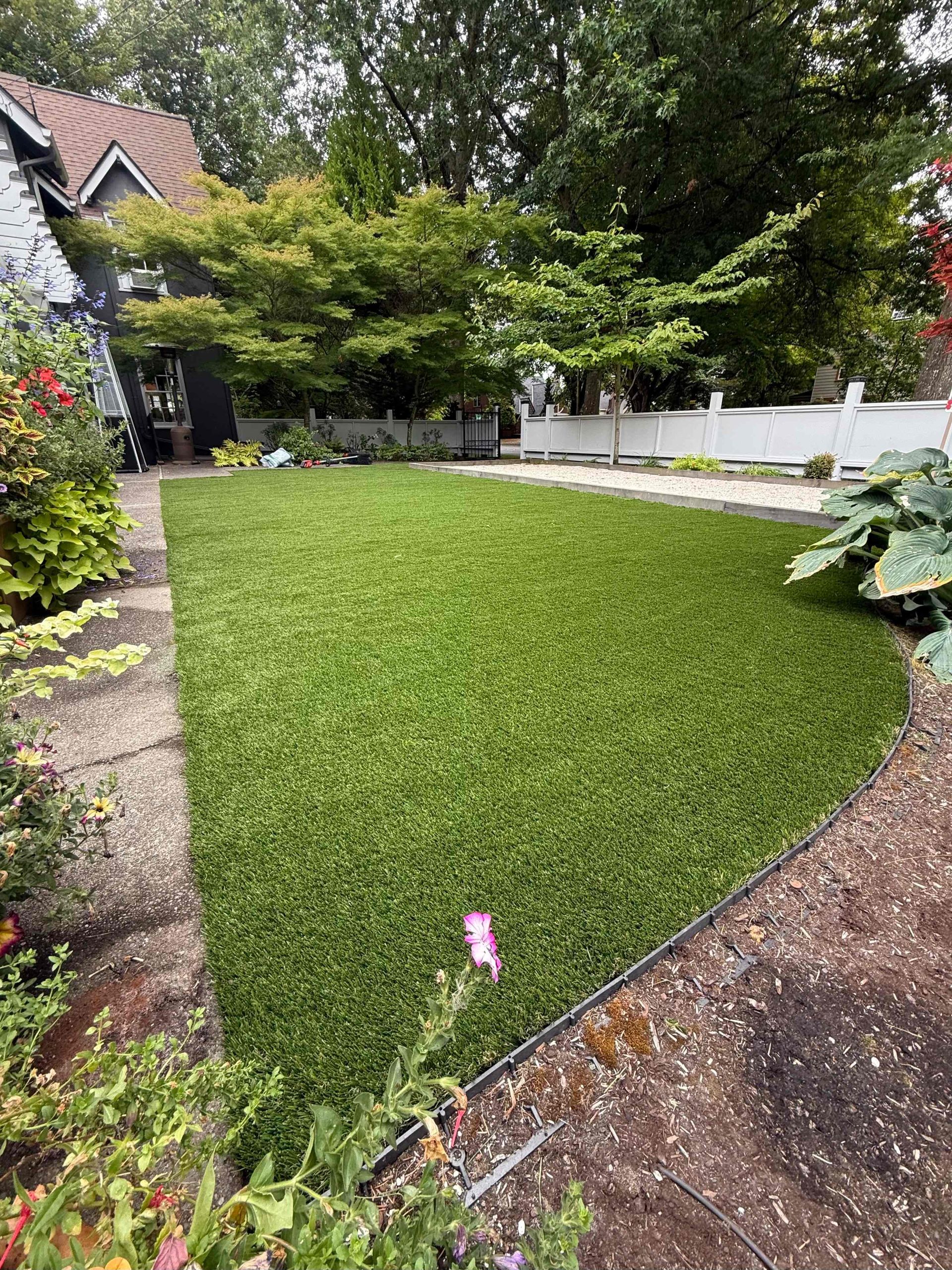 Curved green lawn in a garden with trees, shrubs, and a house in the background