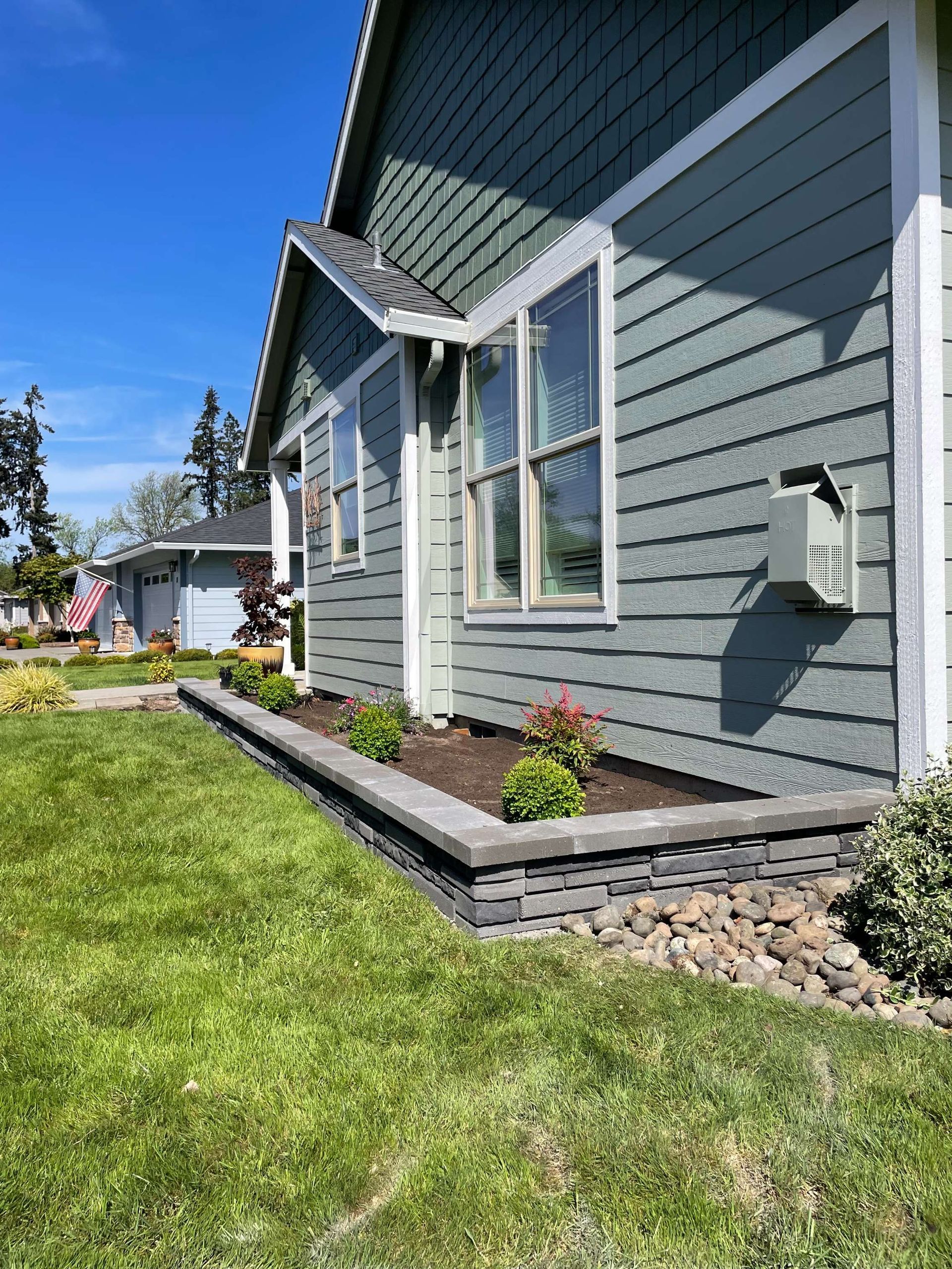Blue house exterior with white-trimmed windows, flower bed, and green lawn on a sunny day