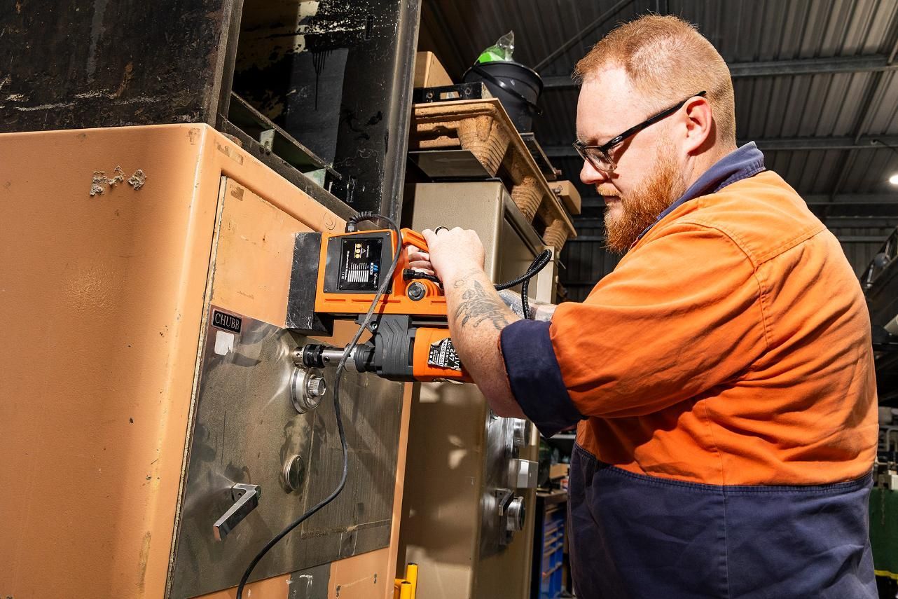 Man in Orange Work Shirt Drills Into Metal — Active 247 Locksmith and Security Services Forster In Forster, NSW