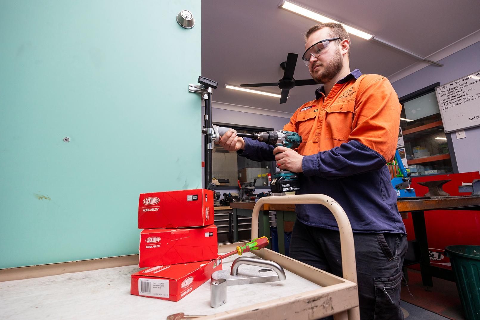 Man in Work Clothes Drilling a Door — Active 247 Locksmith and Security Services Forster In Nabiac, NSW