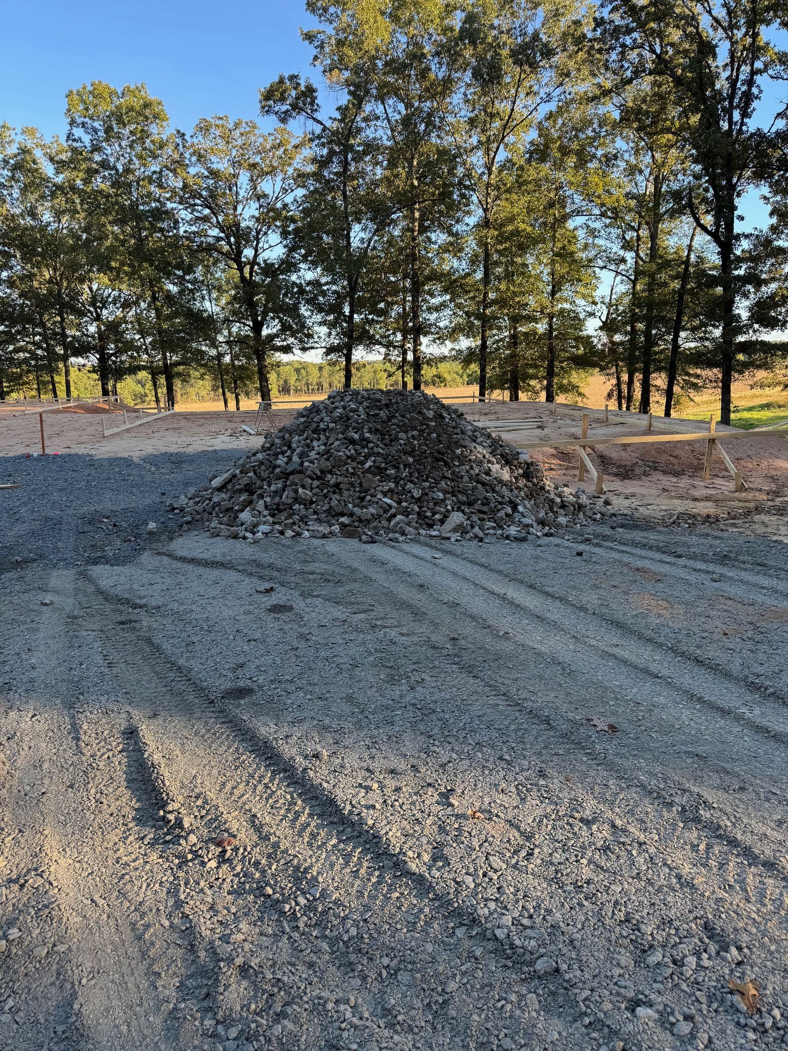 Piles of gravel on a dirt lot with trees in the background at sunset