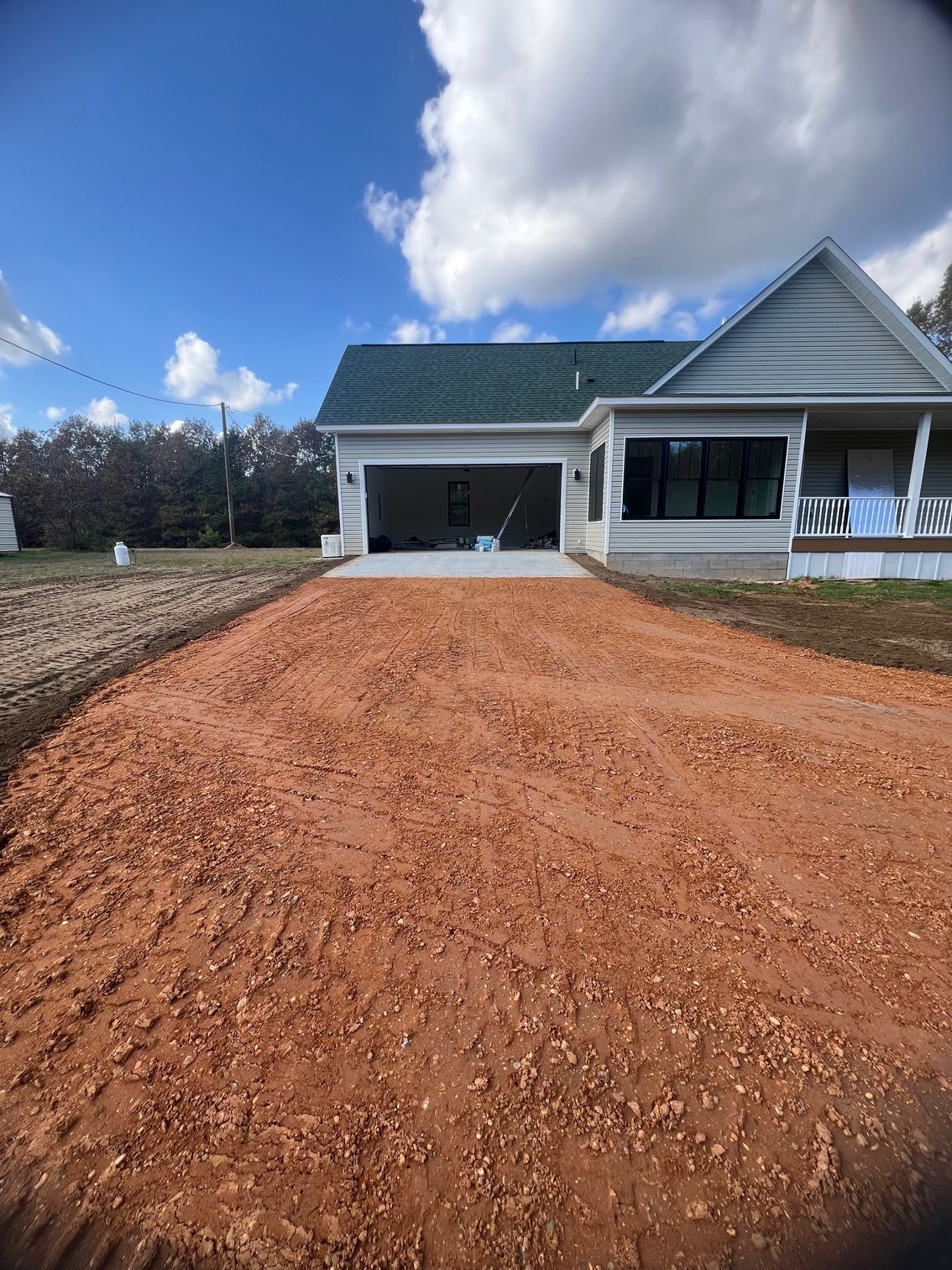 Gravel driveway leading to a white house with a garage under a blue sky with clouds