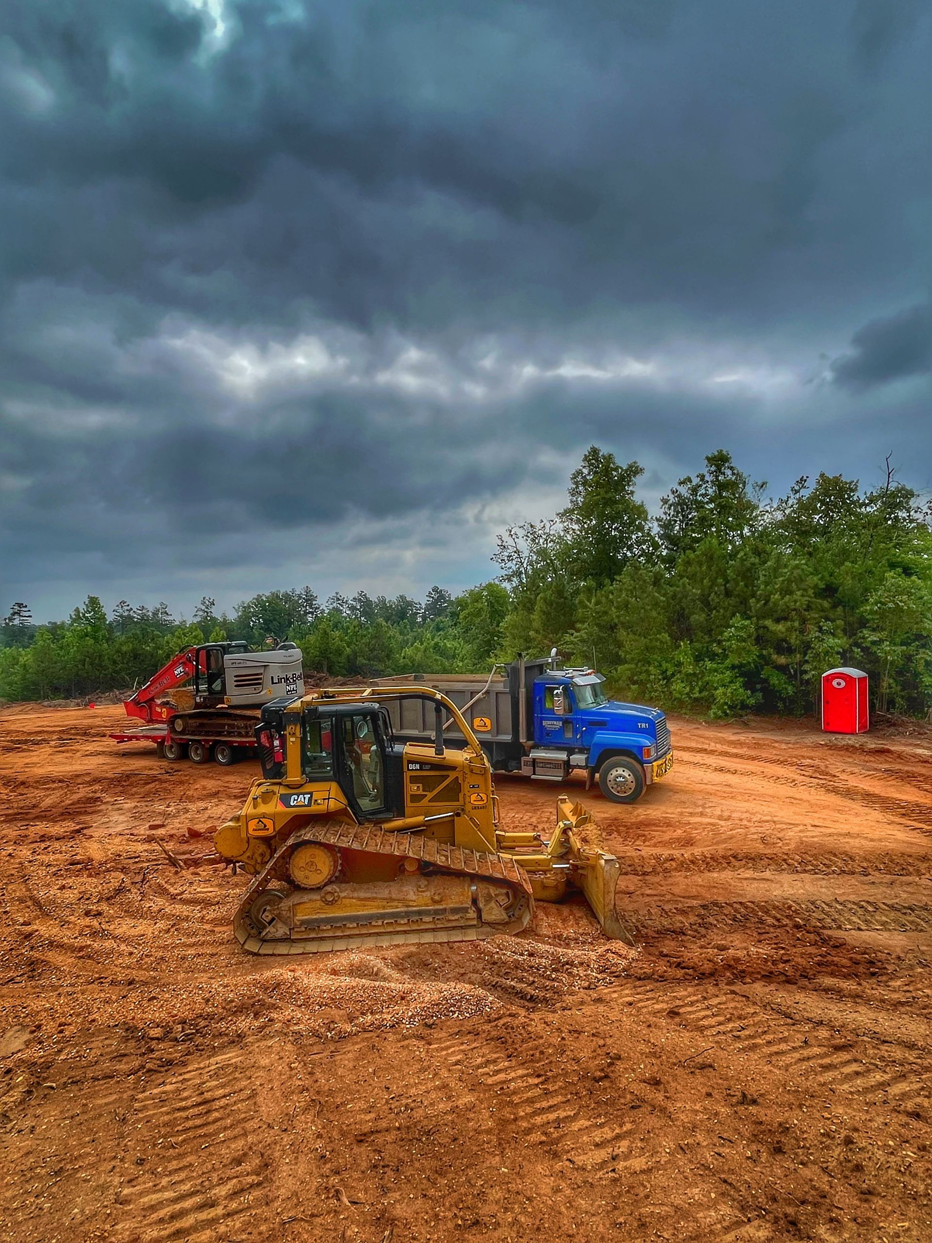 Bulldozers and trucks on a muddy worksite under dark storm clouds