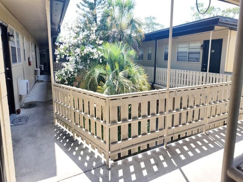 Courtyard with a light beige fence, palm trees, and apartments in the background. Sunny day at Caroline Village in Jacksonville, FL.