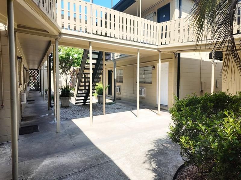 Courtyard with covered walkways, stairs, and small trees and bushes in an apartment complex at Caroline Village in Jacksonville, FL.