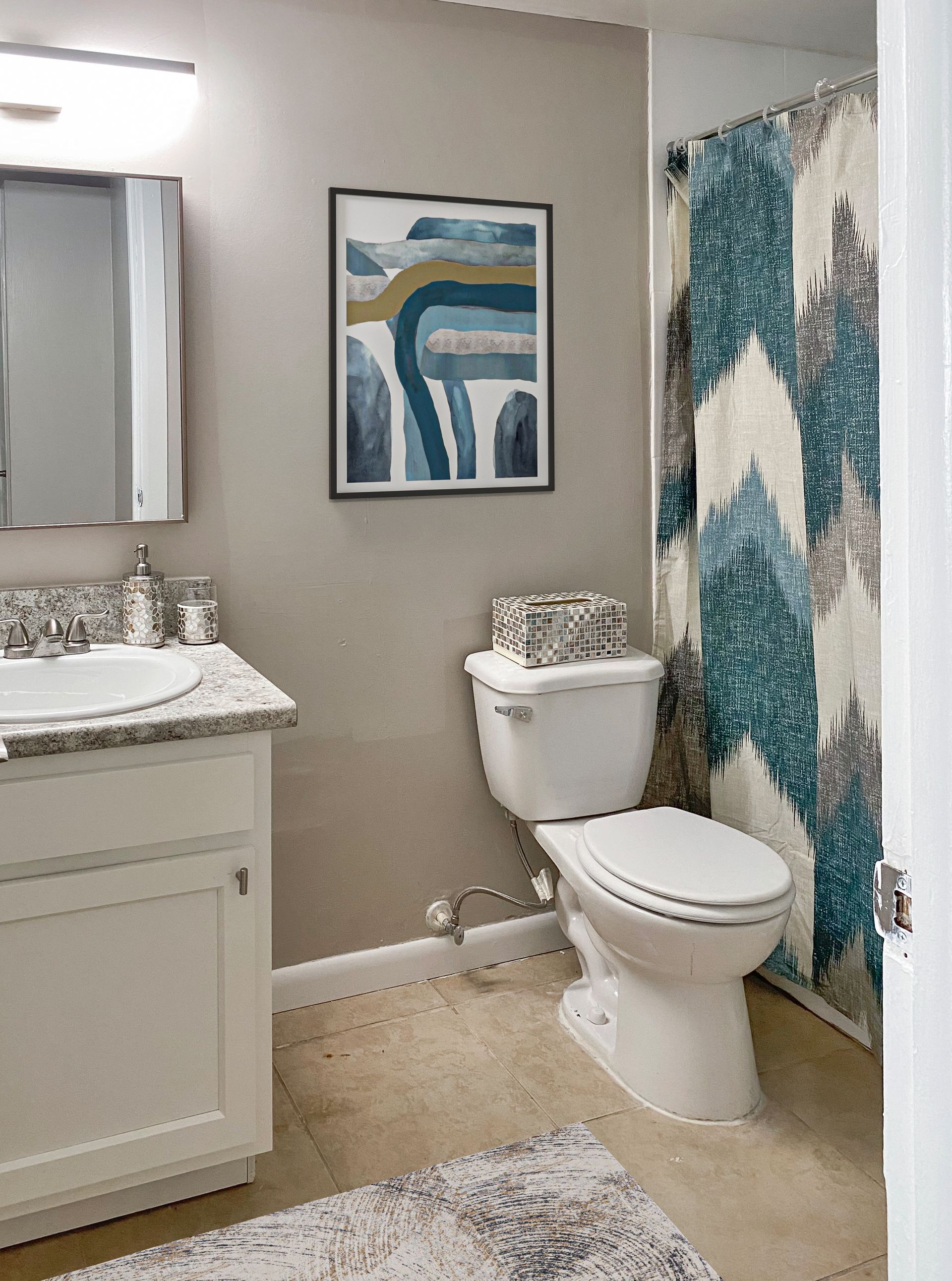 Bathroom with white vanity, toilet, patterned shower curtain, and abstract art at Caroline Village in Jacksonville, FL.