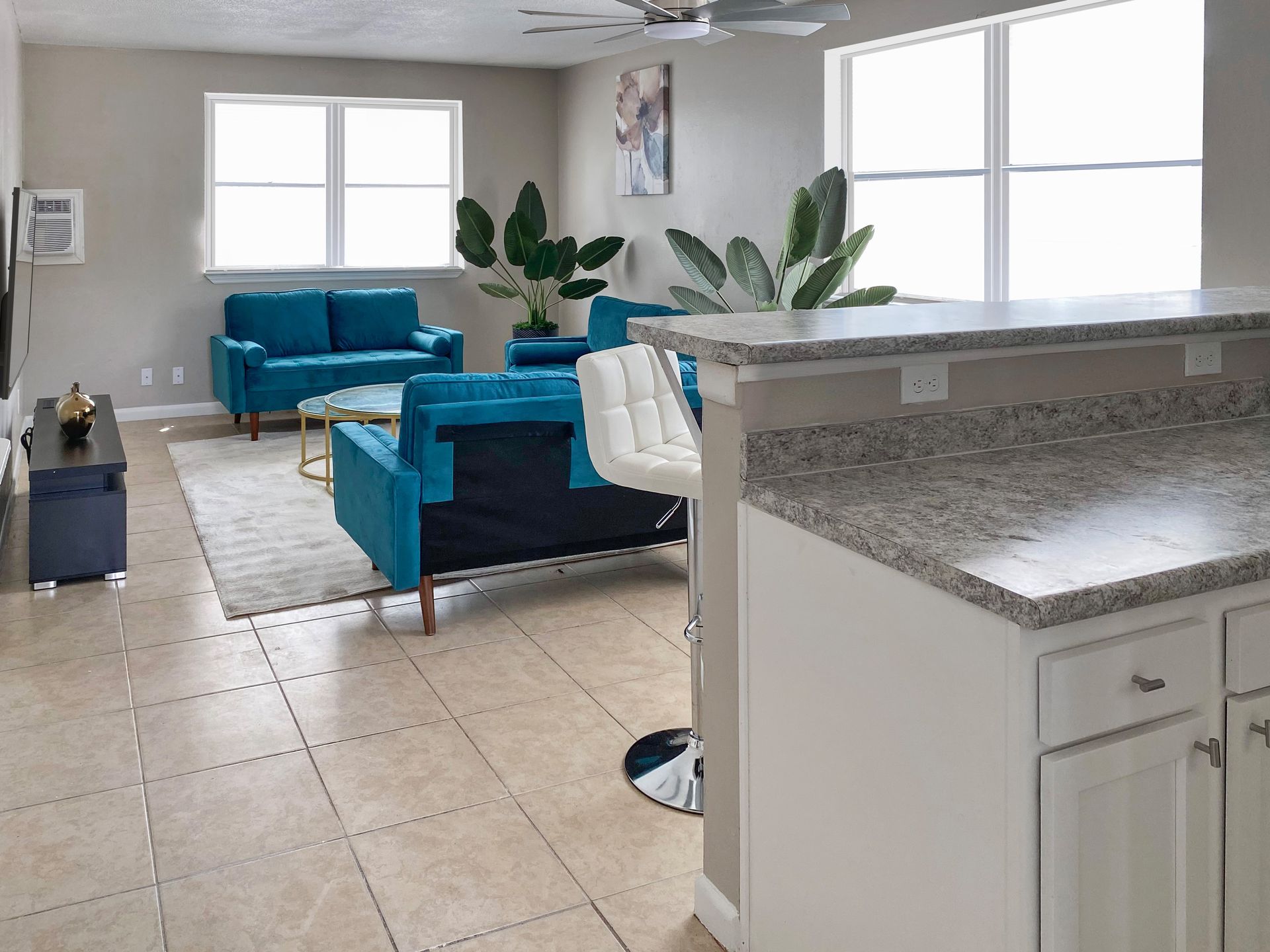 Living room with teal sofas, granite countertop, and large windows at Caroline Village in Jacksonville, FL.