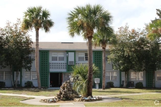 Two-story apartment building with palm trees in a grassy courtyard. Light blue and green exterior at Caroline Village in Jacksonville, FL.