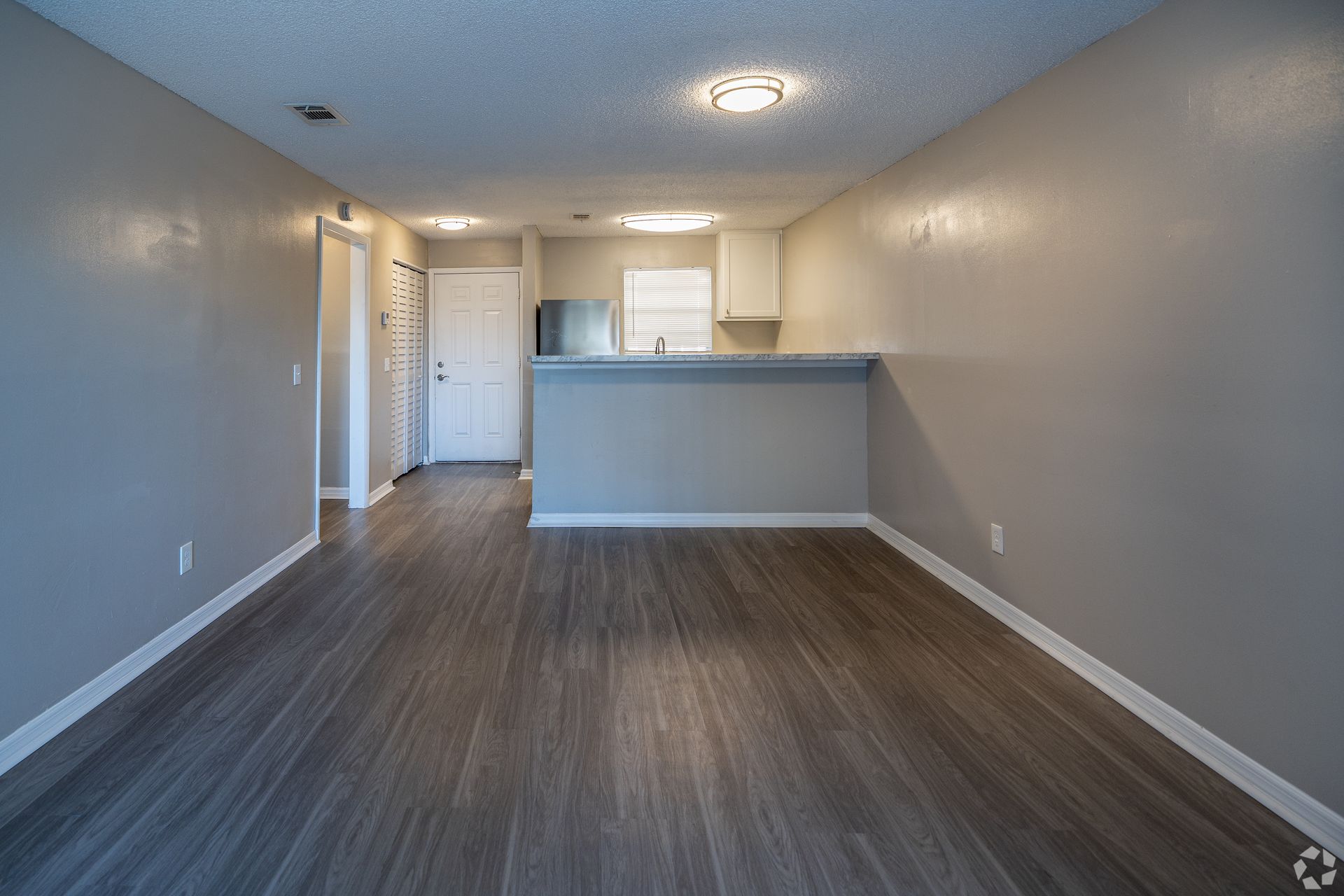 Empty apartment interior, gray walls, wood flooring, kitchen with countertop, open layout at Caroline Village in Jacksonville, FL.