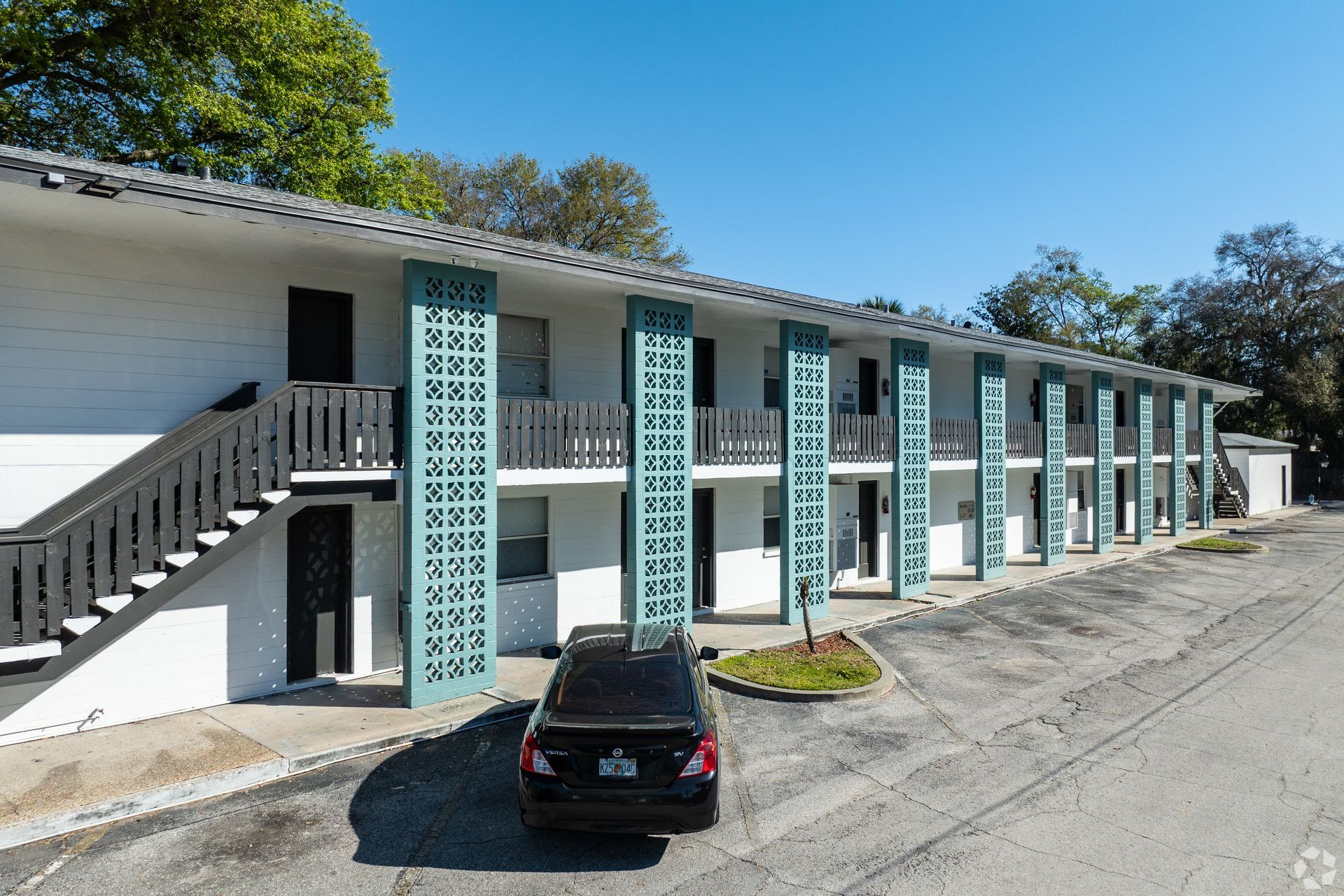 Two-story apartment building with teal accents. A black car is parked in front at Caroline Village in Jacksonville, FL.