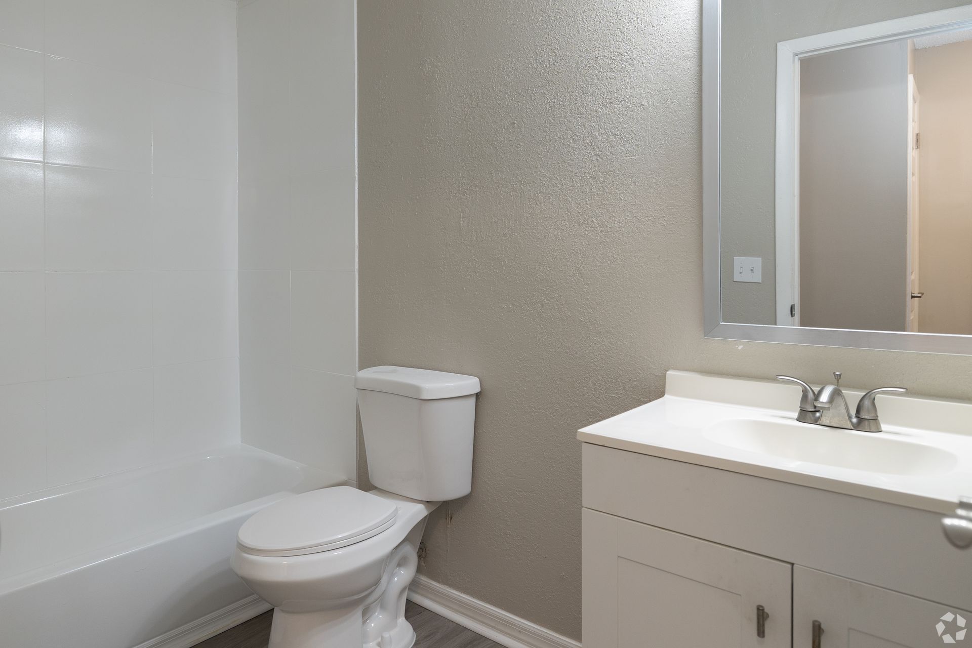 Bathroom with white tub, toilet, vanity, and gray textured wall at Caroline Village in Jacksonville, FL.