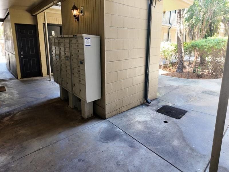 Outdoor hallway with a row of mailboxes mounted on a beige wall at Caroline Village in Jacksonville, FL.