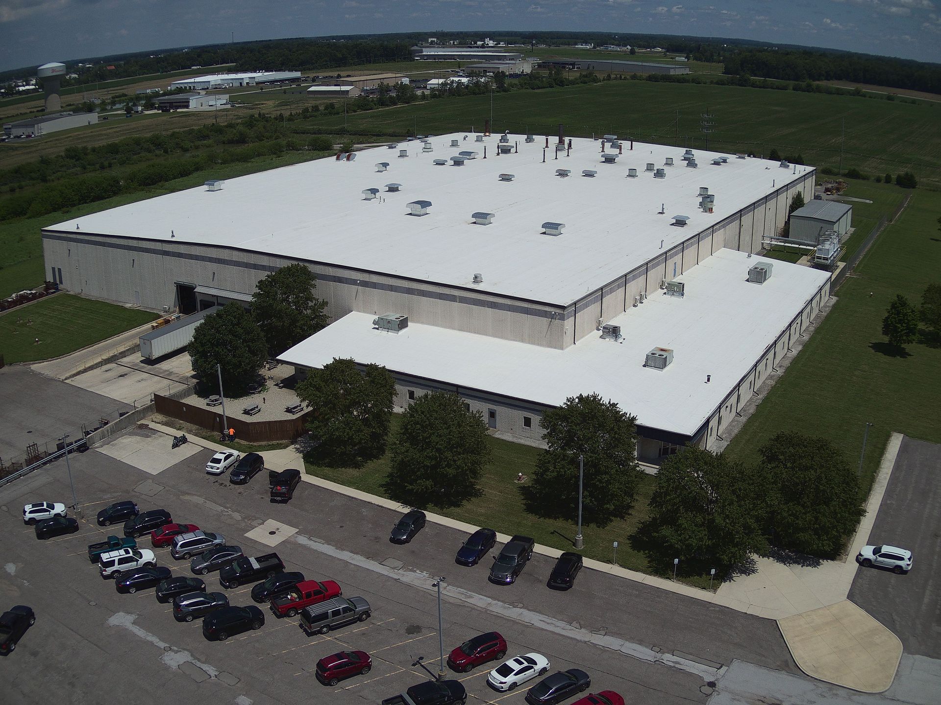 Aerial view of a large white industrial building with a parking lot and surrounding fields