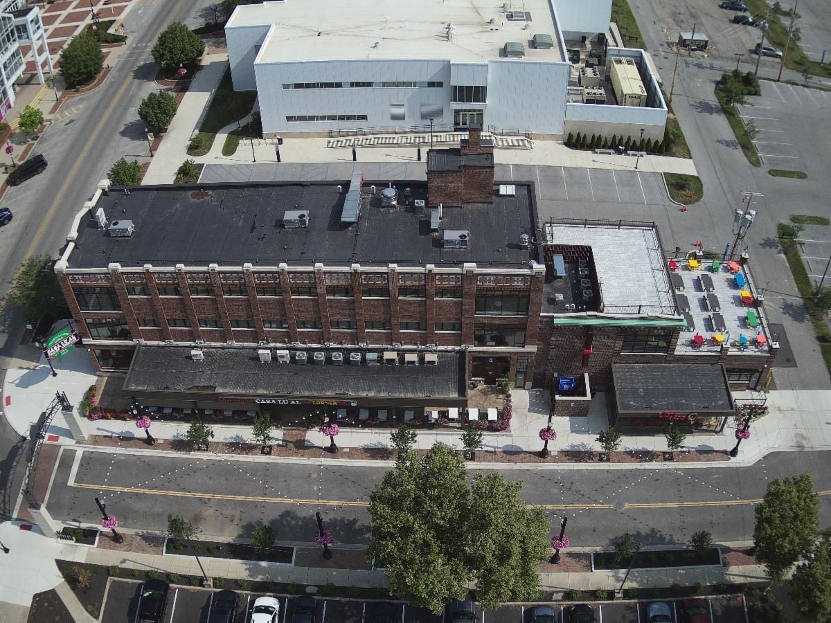 Aerial view of a brick building on a city street with a colorful rooftop patio and nearby parking lot.
